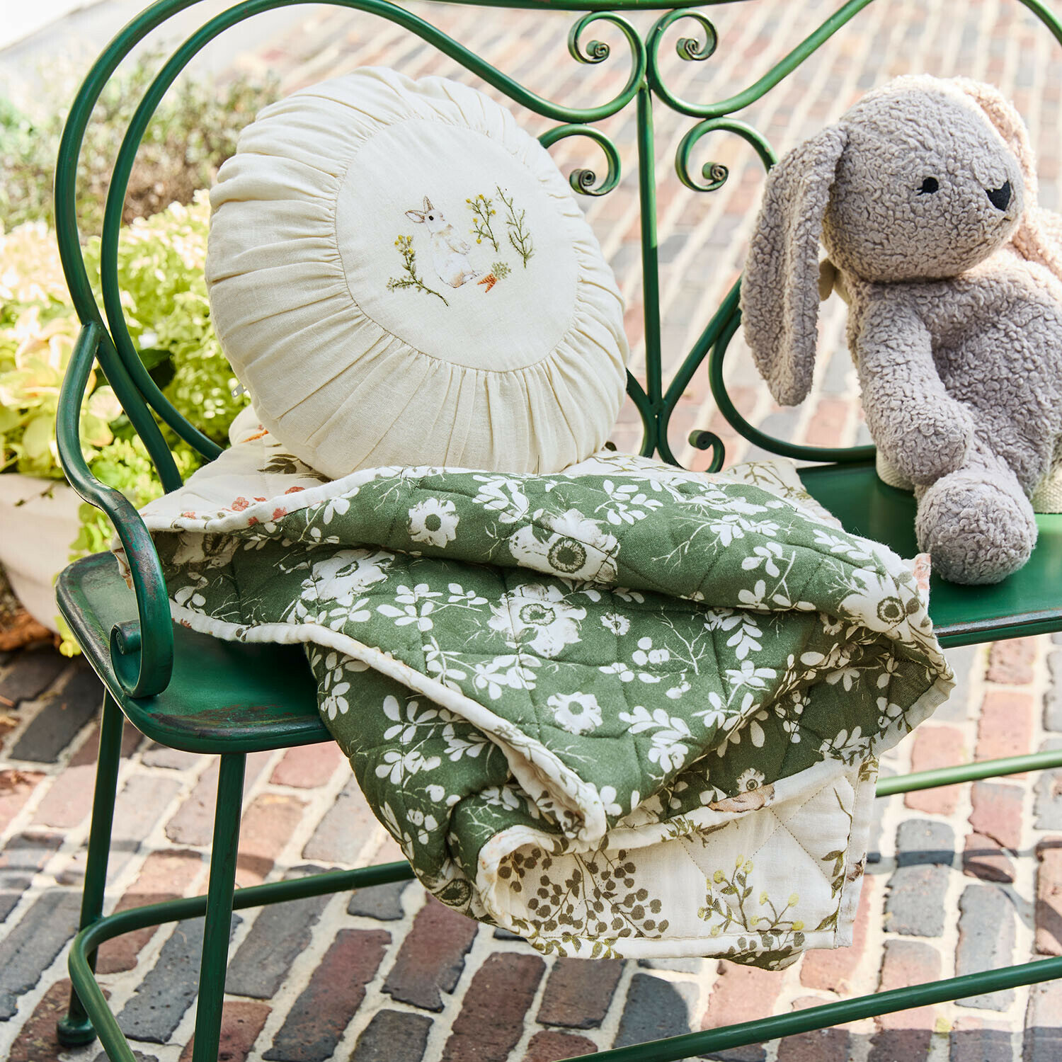 Grüne gesteppte Decke mit weißem Blumenmuster auf grünem Metallbank mit rundem Kissen und Plüschhase