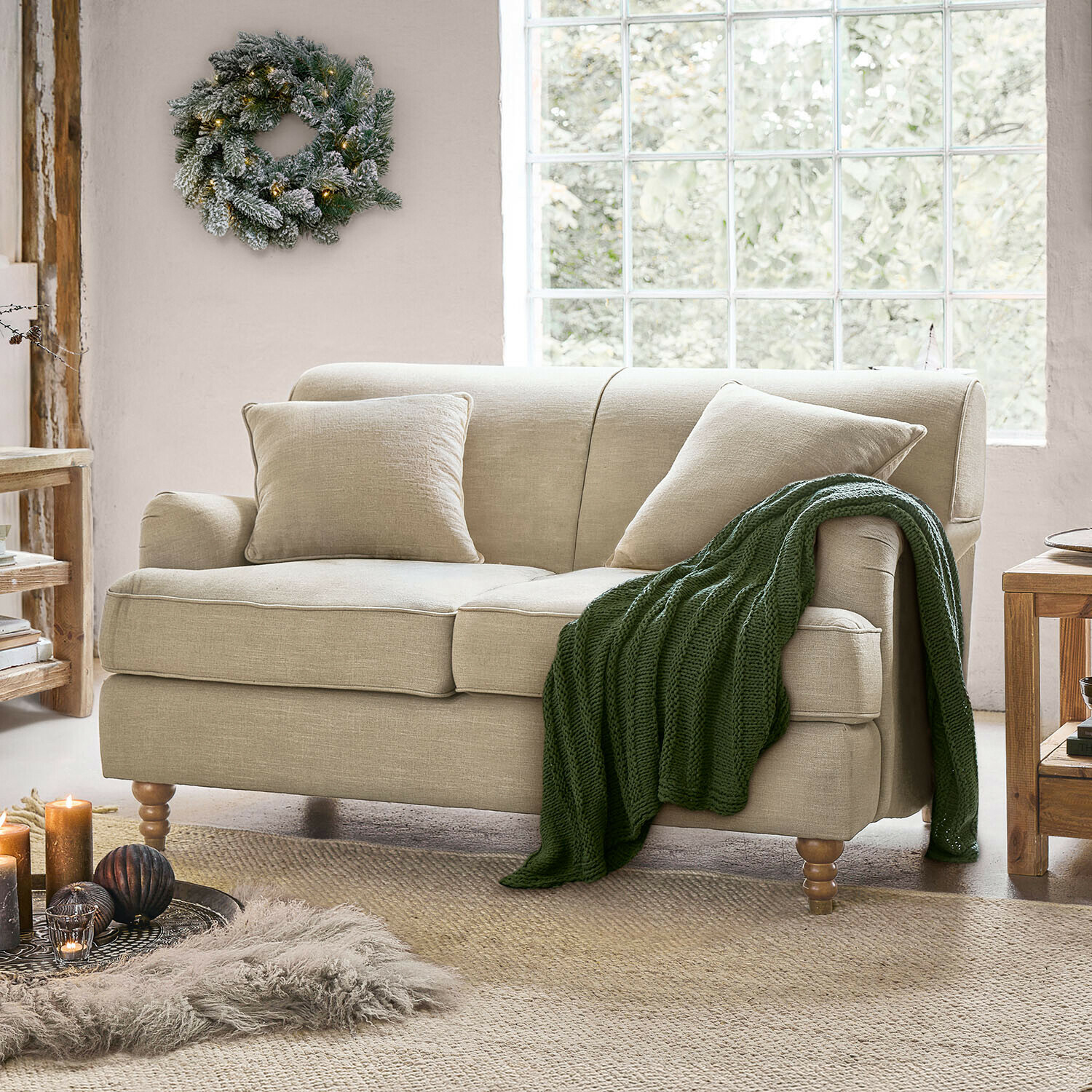 Sofa Isa Beiges Sofa aus Stoff mit Kissen und gestrickter Decke in hellem Wohnzimmer mit großem Fenster