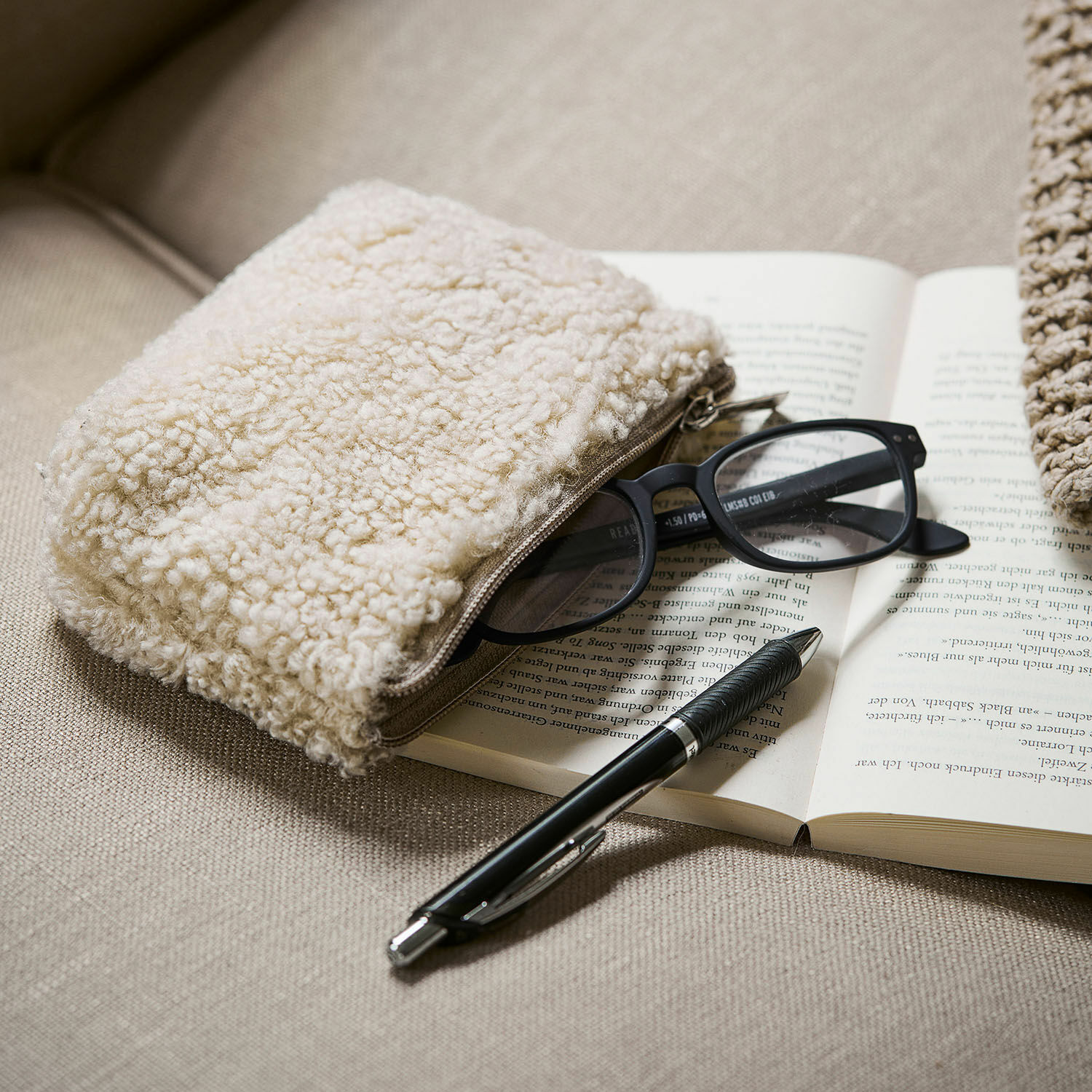 Täschchen Bathilde Beige Kosmetiktasche aus Teddy-Material auf Sofa mit Brille und schwarzem Kugelschreiber