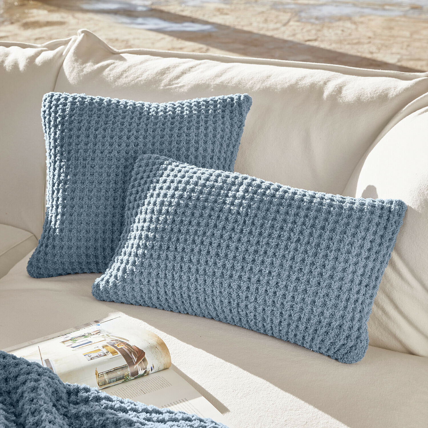 Kissenhülle 2er Set Ysilda Zwei blaue Strickkissen auf cremefarbenem Sofa, weiche Wohnaccessoires für gemütliches Wohnzimmer