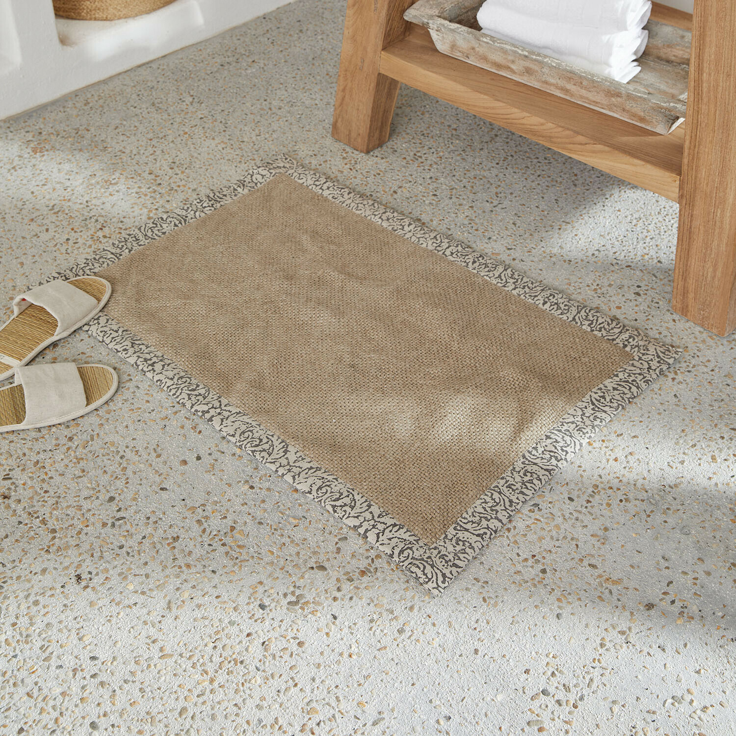 Badematte Falmont Beiger Teppich aus Naturmaterial mit dekorativem grauem Rand auf hellem Steinfussboden