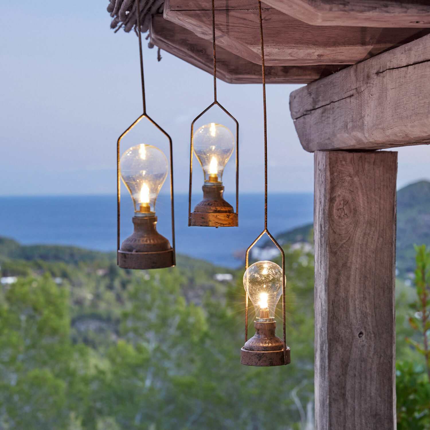 LED-Hängelaterne 3er Set Chambéry Drei hängende Metalllampen mit Glühbirnen vor grünem Wald und Meer, Außenbeleuchtung