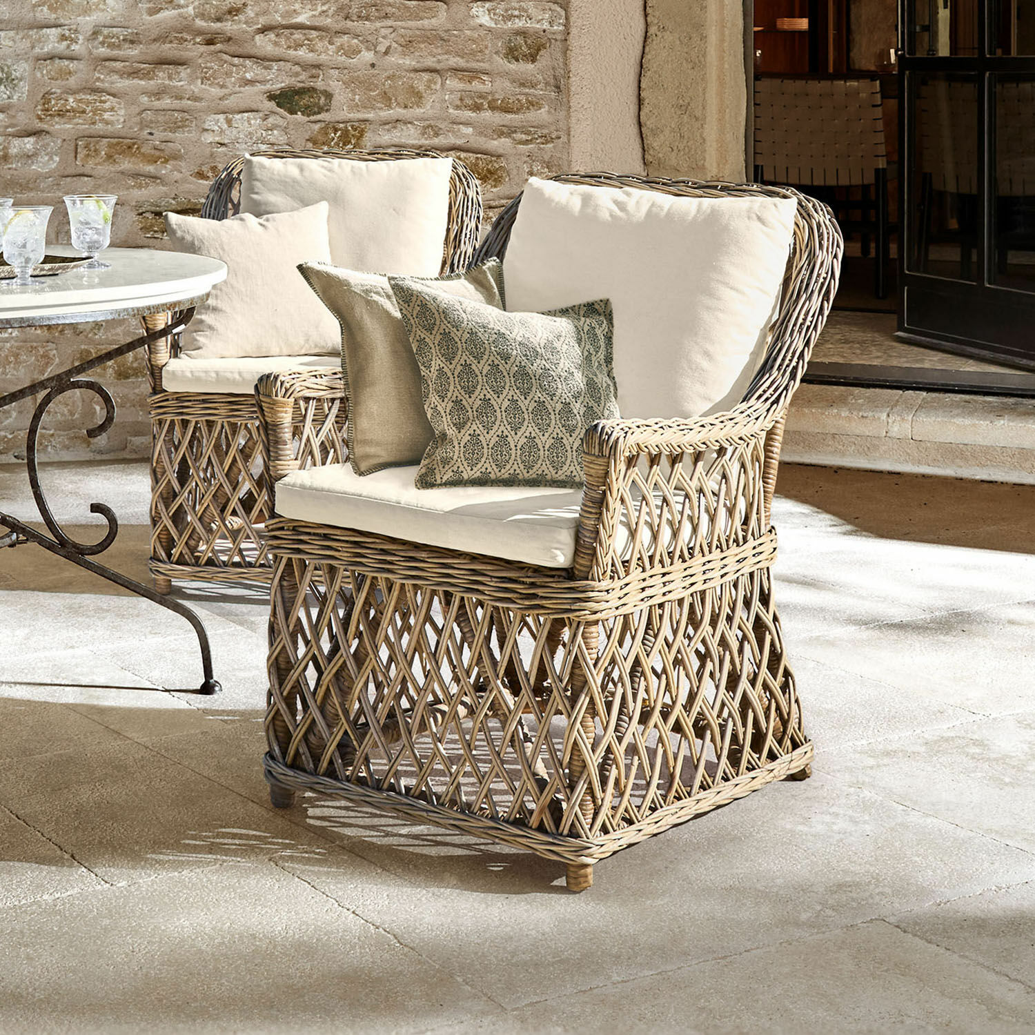 Sessel Nesvryn Bequemer Sessel aus natürlichem Rattan mit cremefarbenen Polstern und dekorativen Kissen für Terrasse.
