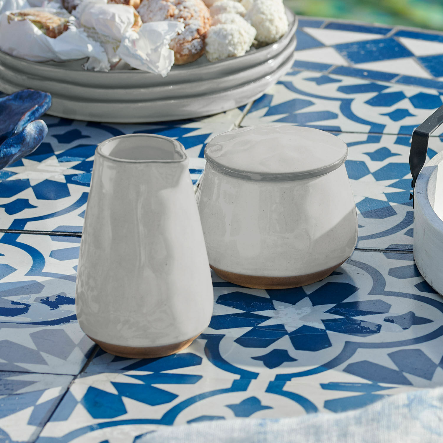Zuckerdose und Milchkännchen Biarré Weiße Keramik-Kanne und Zuckerdose mit braunem Naturboden auf blau-weiß gefliestem Tisch