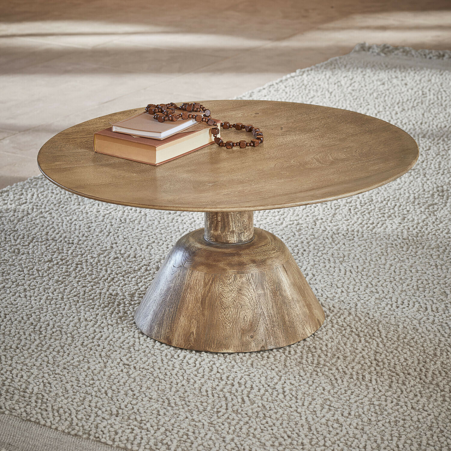 Couchtisch Ulric Runder Couchtisch aus Holz in Naturfarbe auf hellem Teppich mit Büchern und Perlenkette