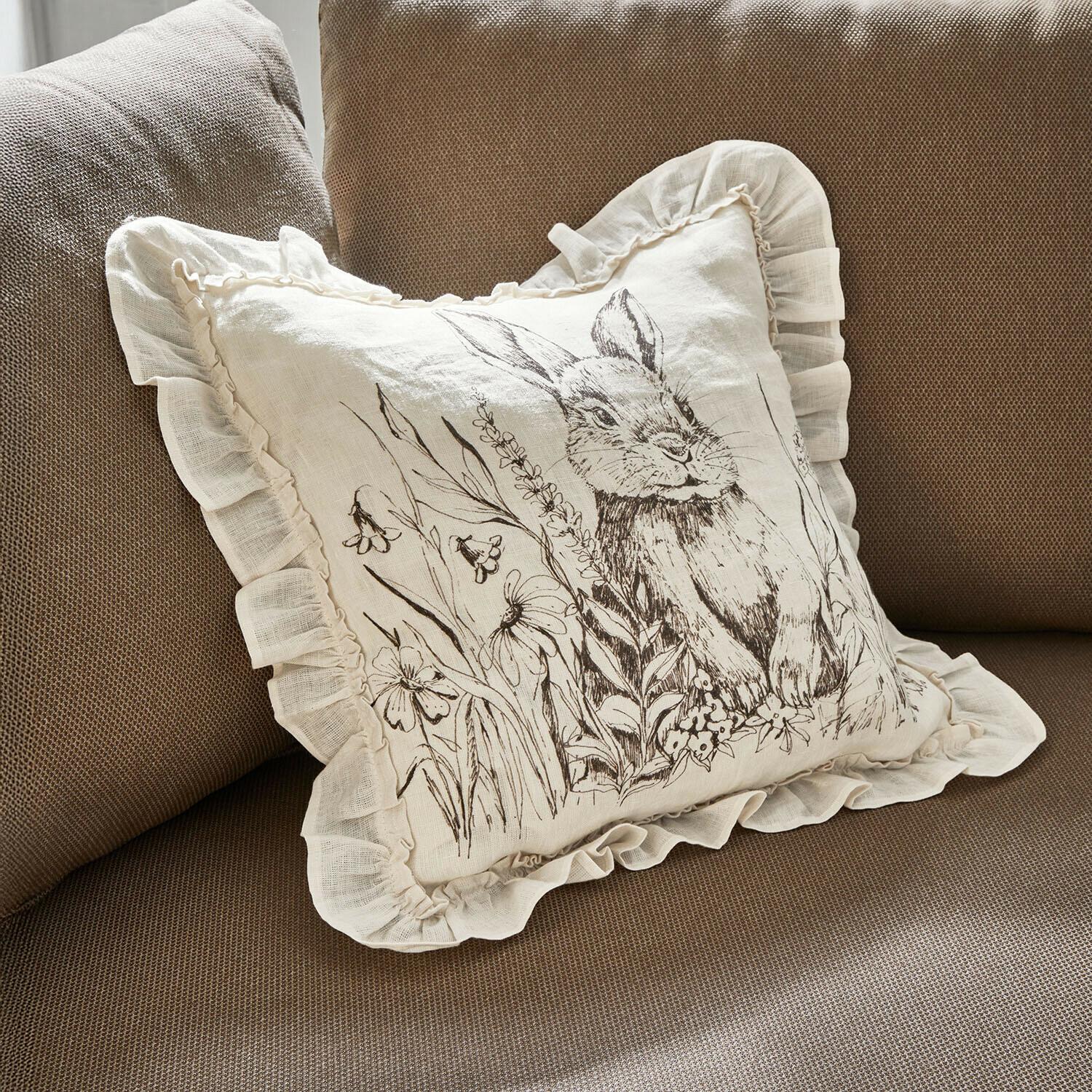 Kissenhülle Brionelle Beige Leinenkissen mit Rüschen und Hasenmotiv mit Blumen auf braunem Sofa