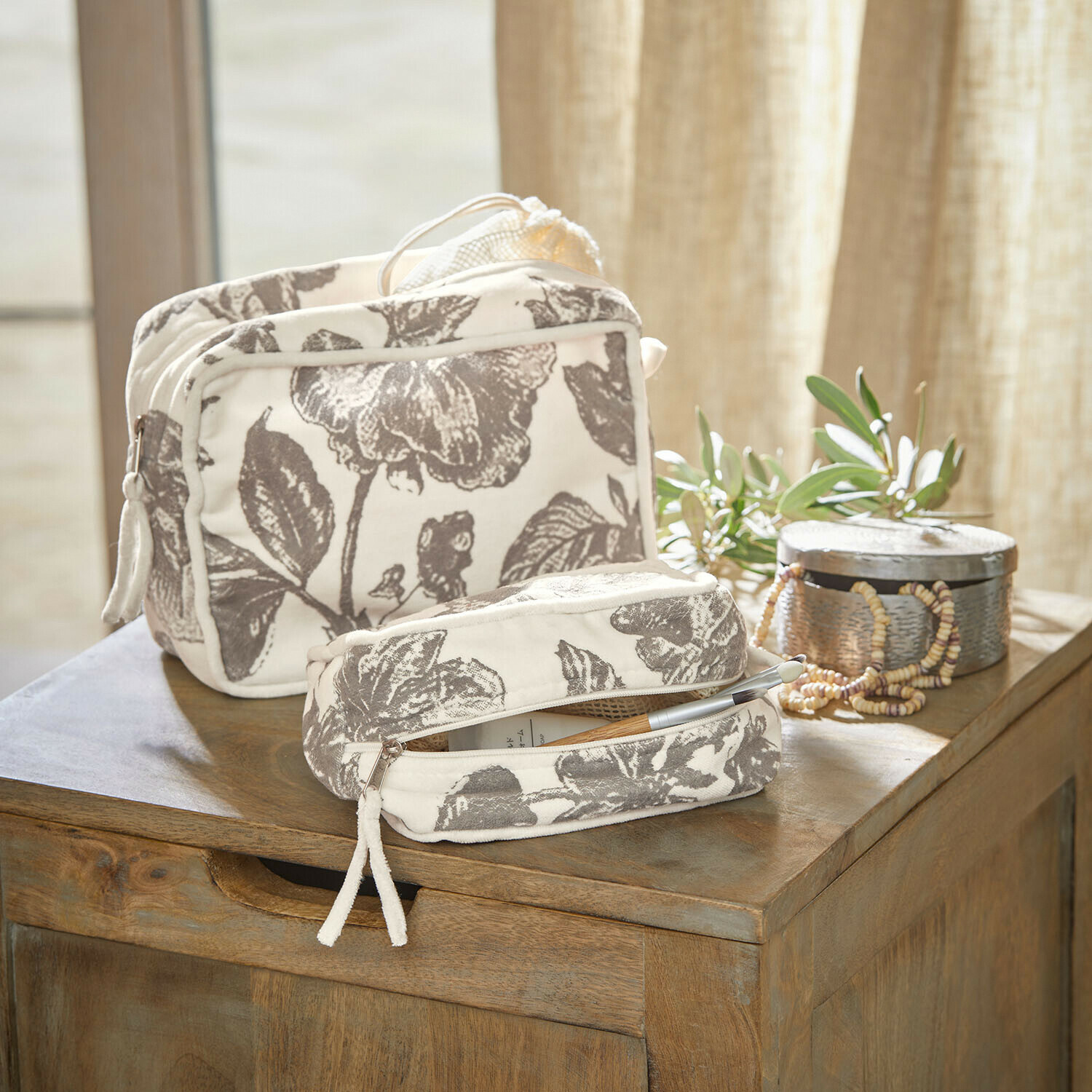 Täschchen 2er Set Brilonne Set aus zwei cremefarbenen Baumwoll-Kosmetiktaschen mit grauem Blumenmuster auf Holztisch