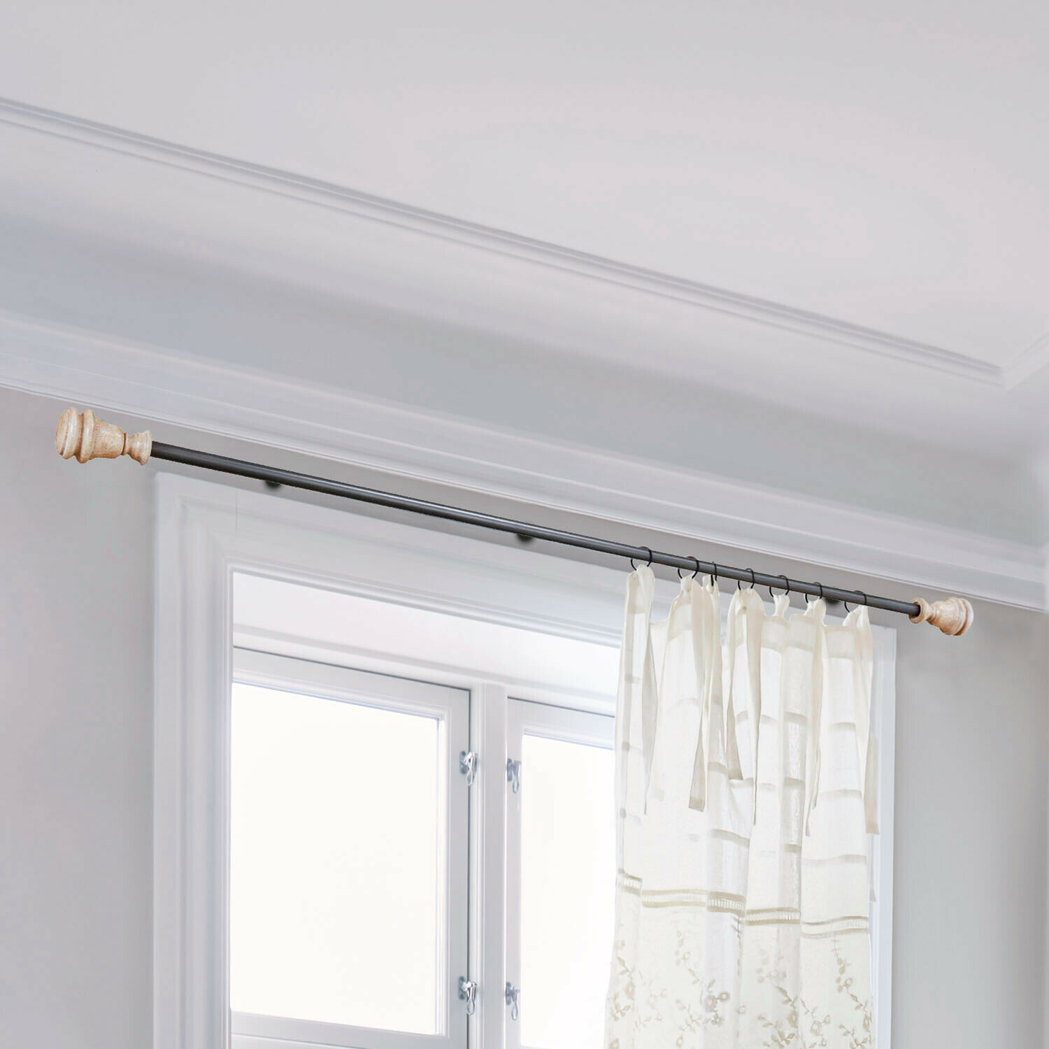 Schwarze Metall-Gardinenstange mit hellen Holzenden und weißem besticktem Vorhang am Fenster