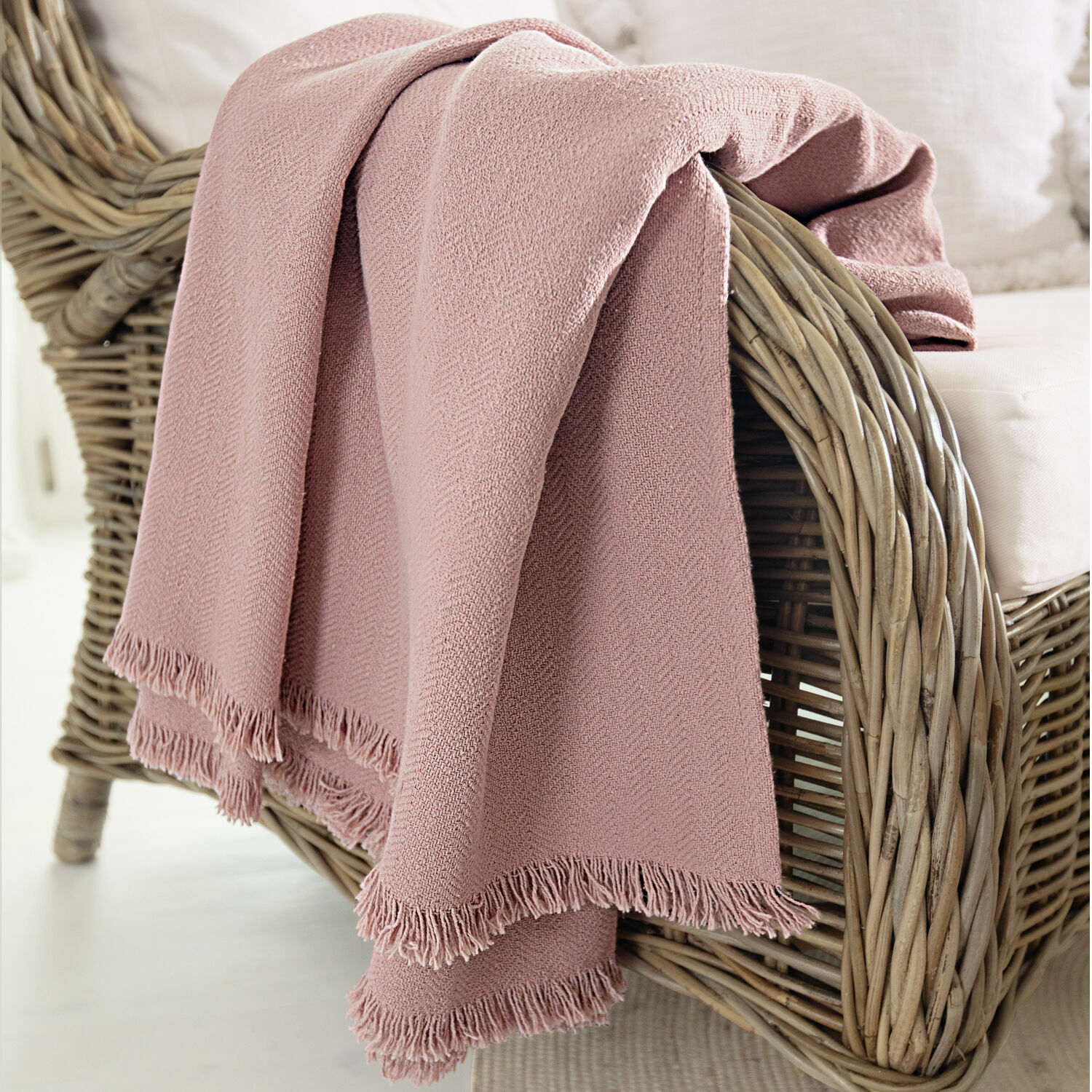 Plaid Herepian Rosa Kuscheldecke aus weichem Material mit Fransen auf einem Rattansessel im Wohnzimmer