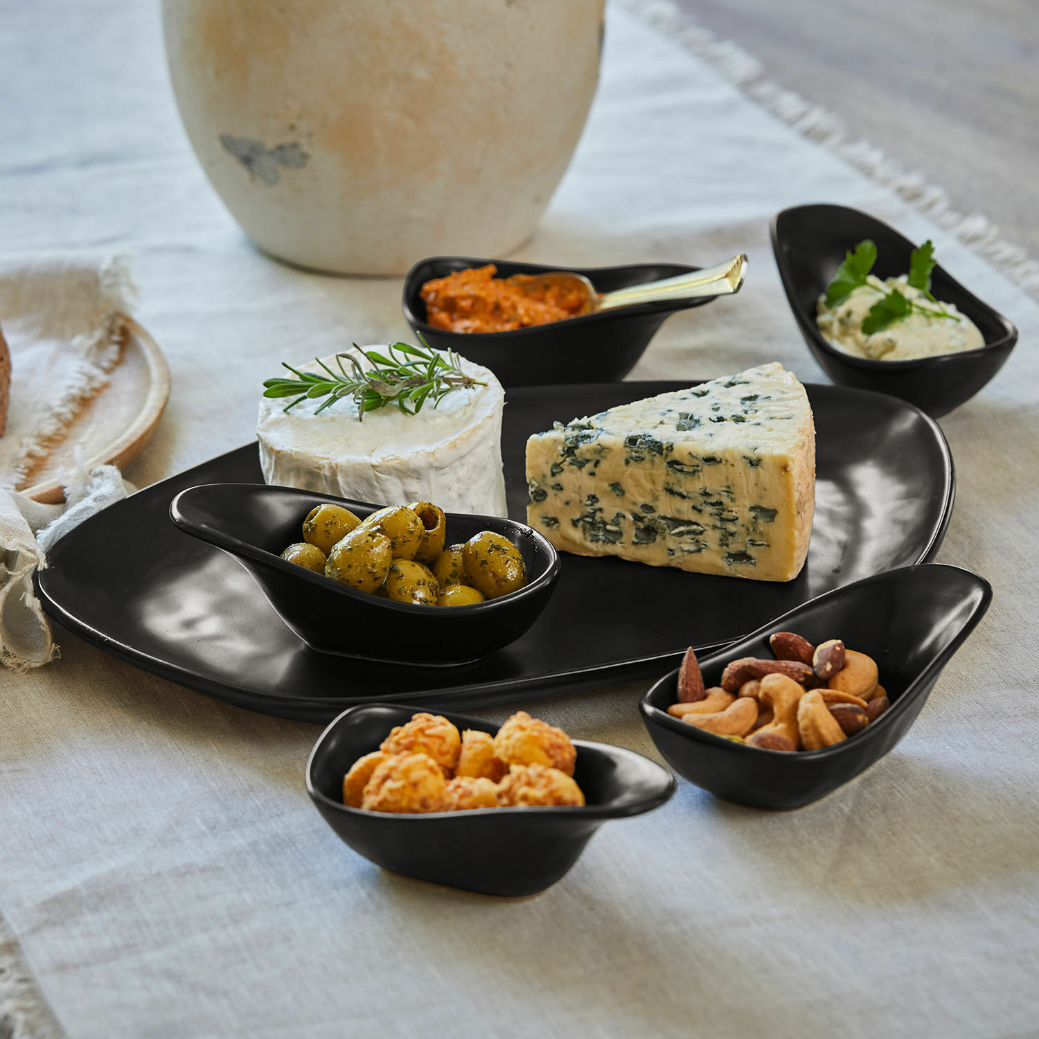 Schwarzes Keramik-Servierset mit Käse, Oliven und Nüssen auf Leinentischdecke
