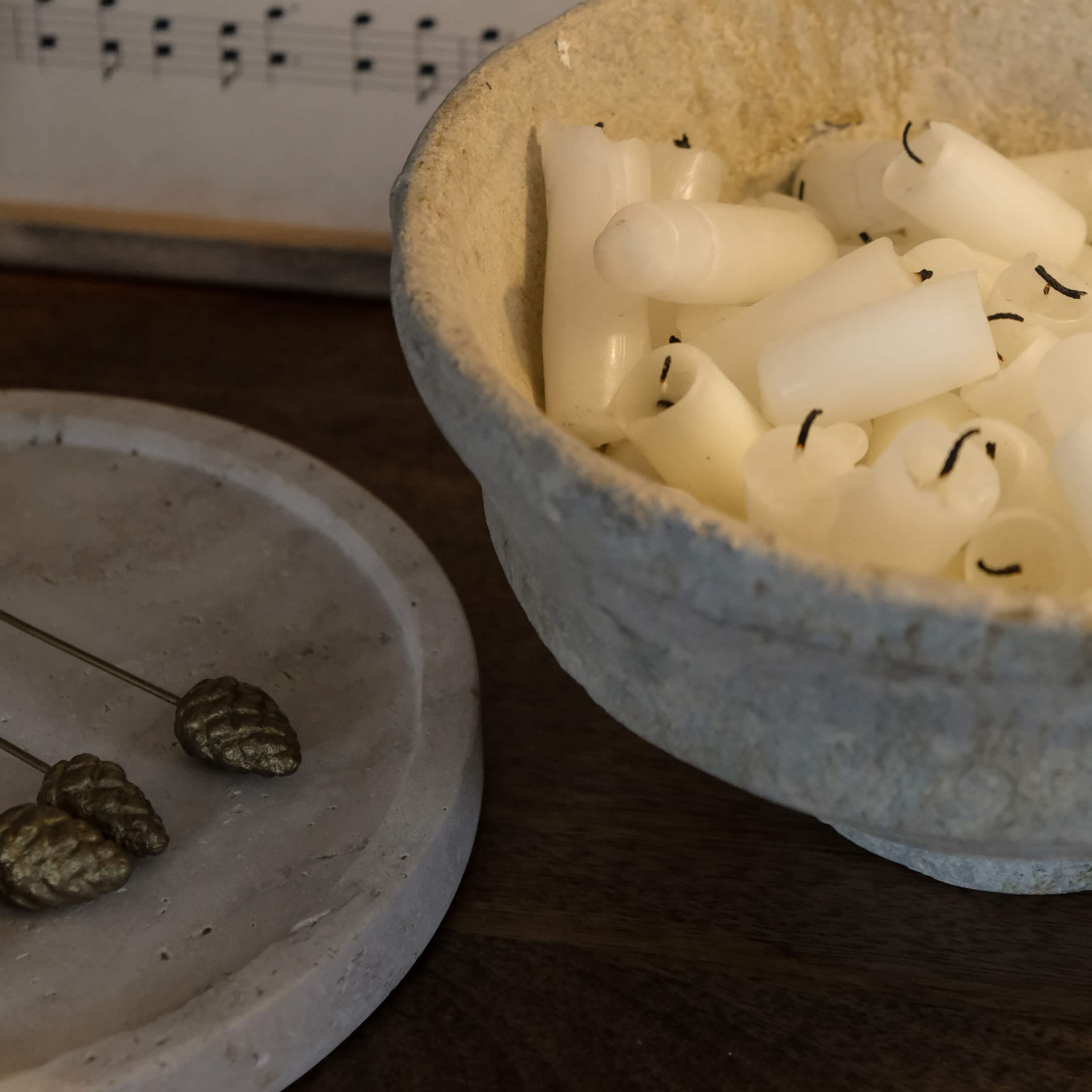Schale aus Naturmaterial mit weißen Kerzen auf dunklem Holztisch, stimmungsvolle Dekoration
