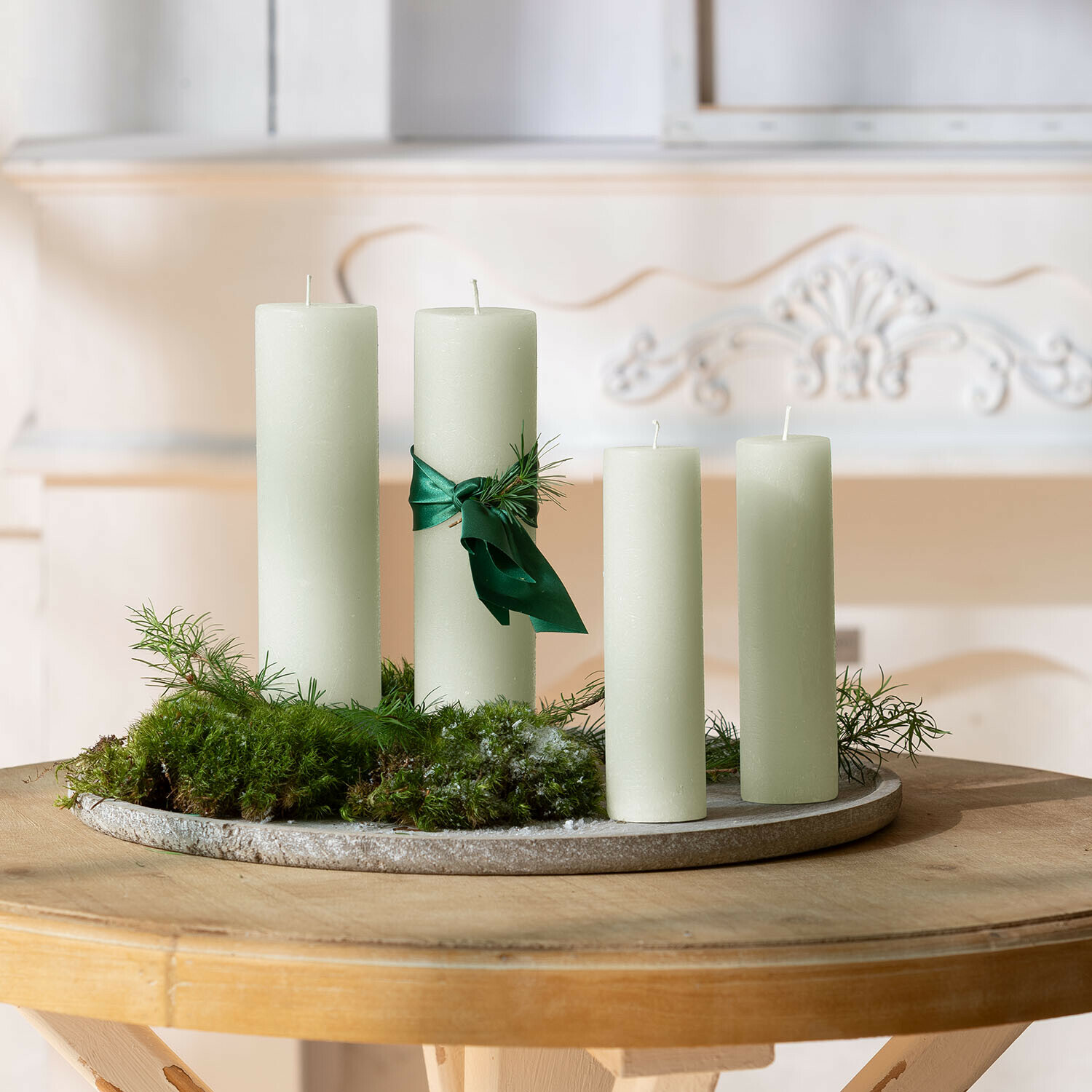 Set aus vier cremefarbenen Kerzen mit grünem Band und Moos auf rundem Dekotablett