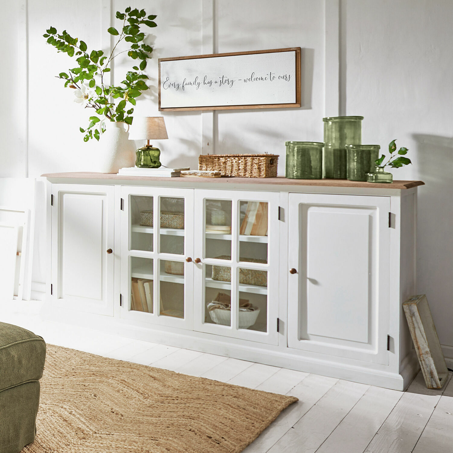 Kommode Kostan Weiße Holzkommode mit Glastüren und hellem Holzplatte in einem hellen Wohnzimmer