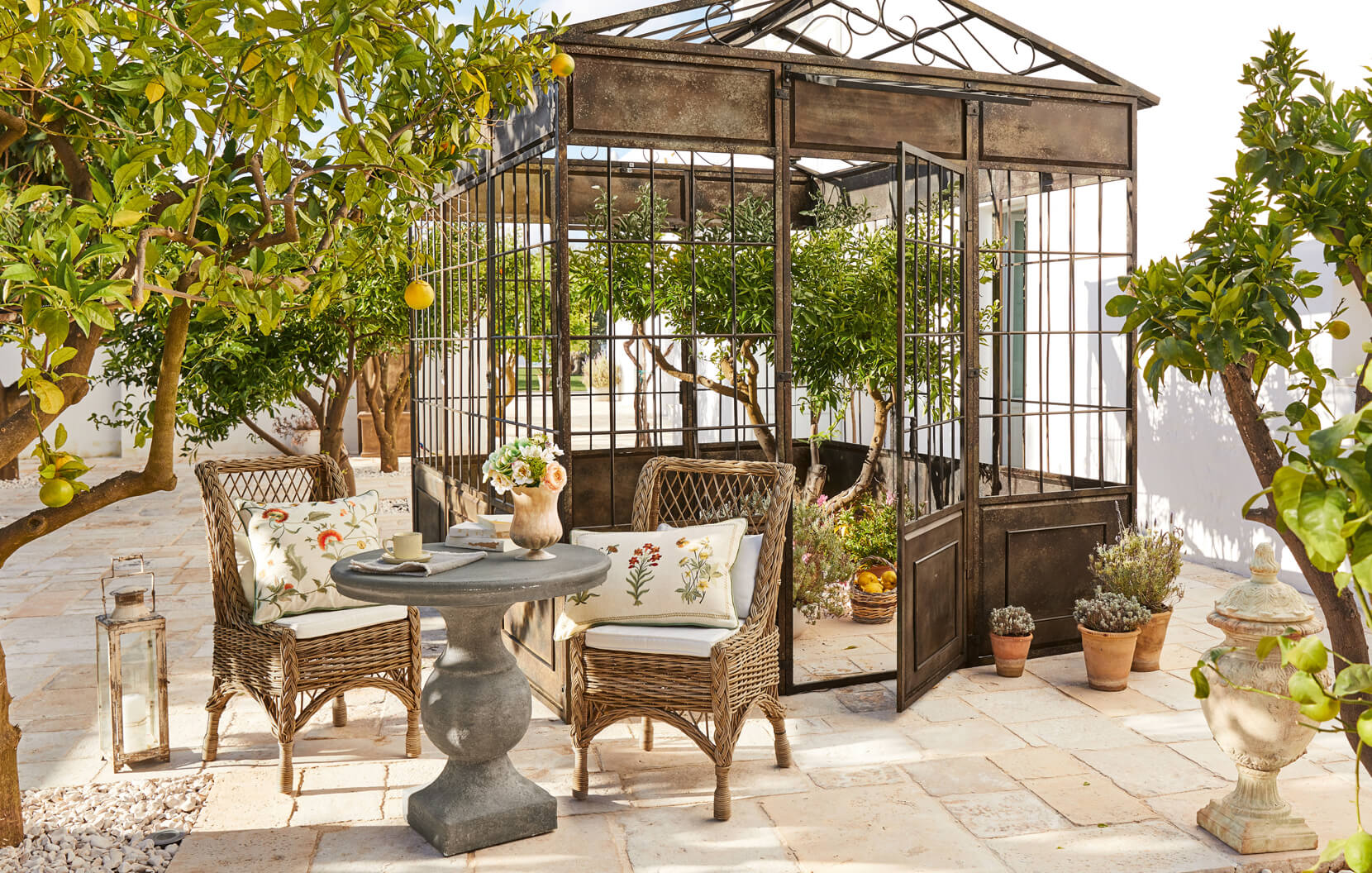 Mediterraner Garten mit Metallpavillon, Rattanstühlen und Steintisch auf der Terrasse