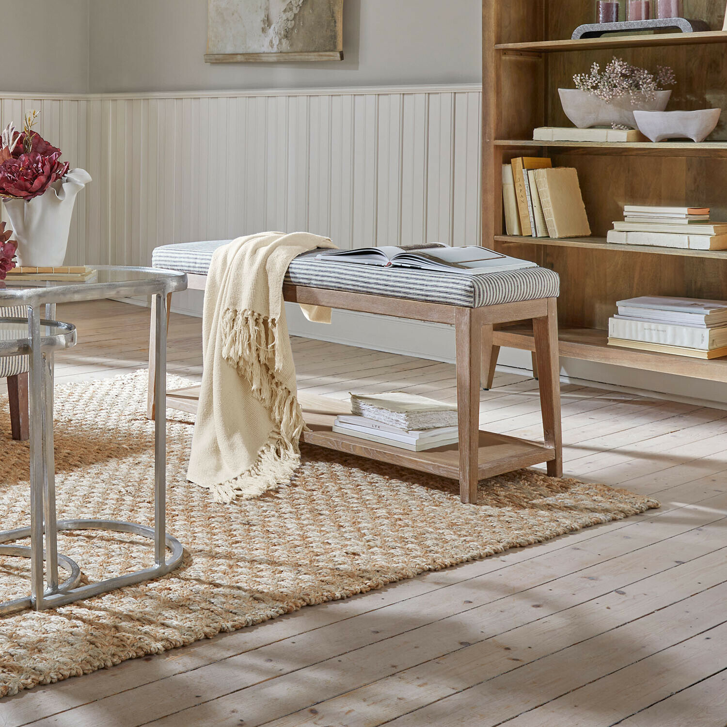 Holzbank mit gepolstertem, gestreiftem Sitz und cremefarbenem Plaid auf natürlichem Teppich