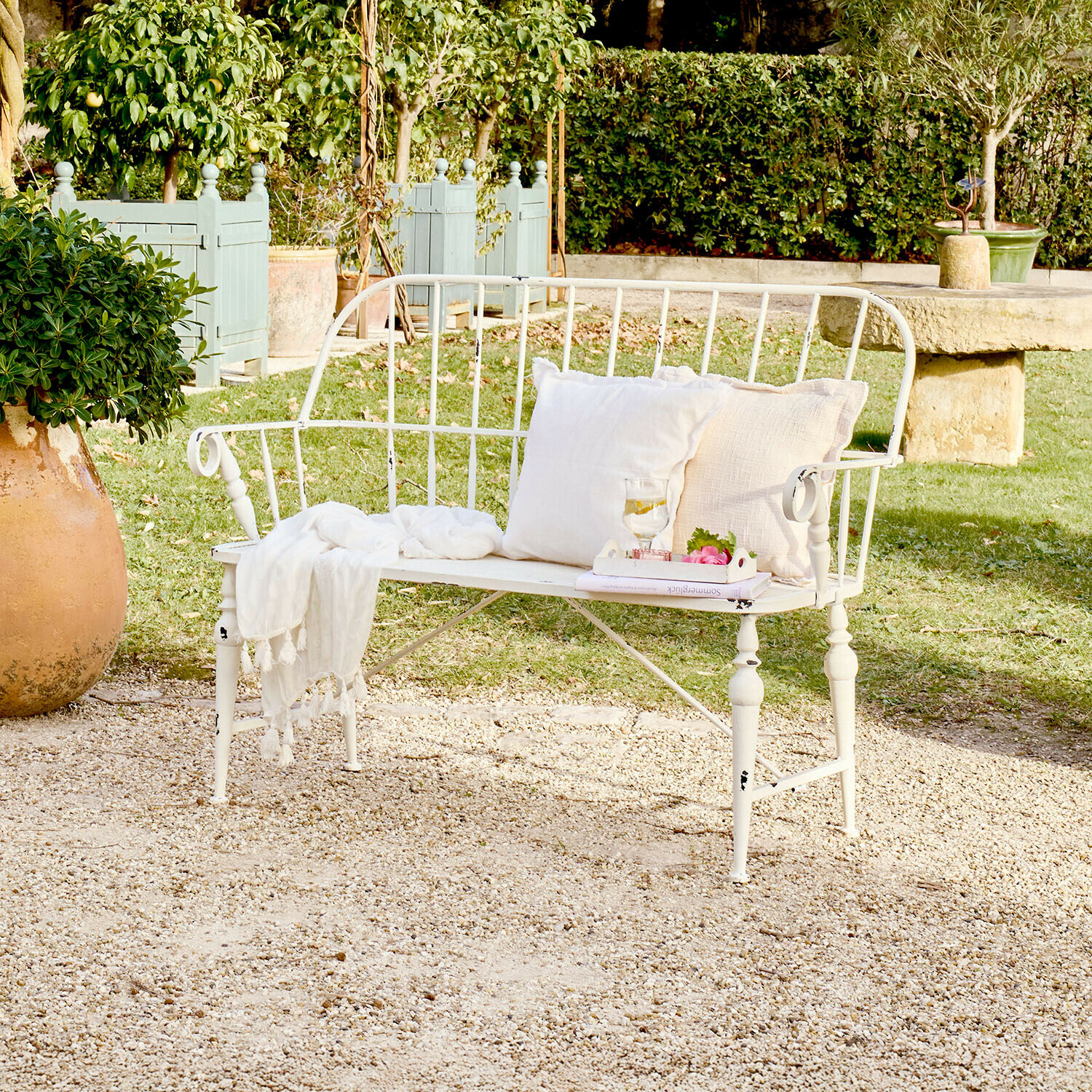 Bank Armingale Weiße Metall-Gartenbank mit Kissen und Decke auf Kiesplatz in grünem Garten