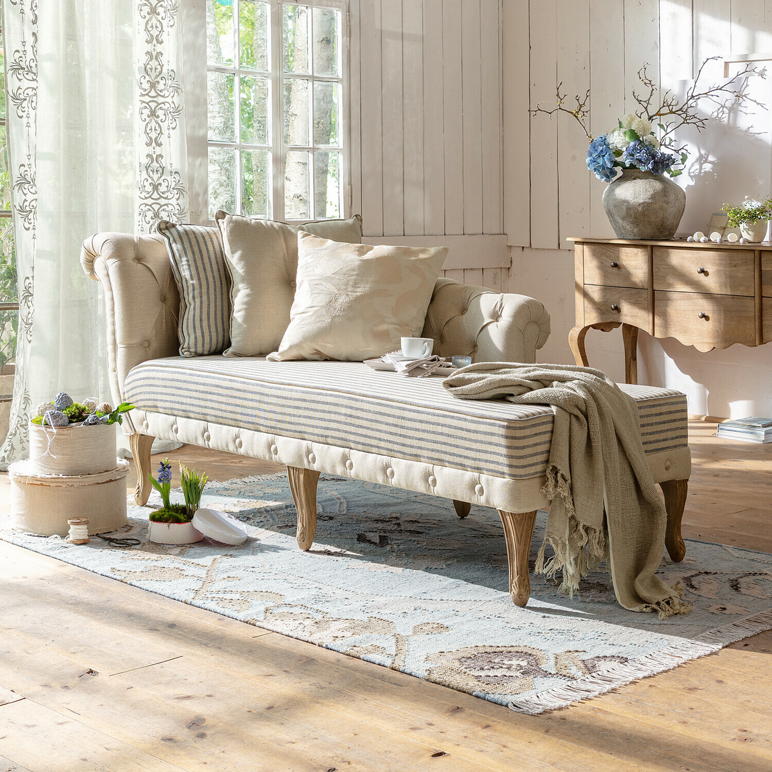 Beige gepolsterte Chaiselongue mit Holzbeinen und gestreiftem Sitz in hellem Wohnzimmer mit Dekokissen