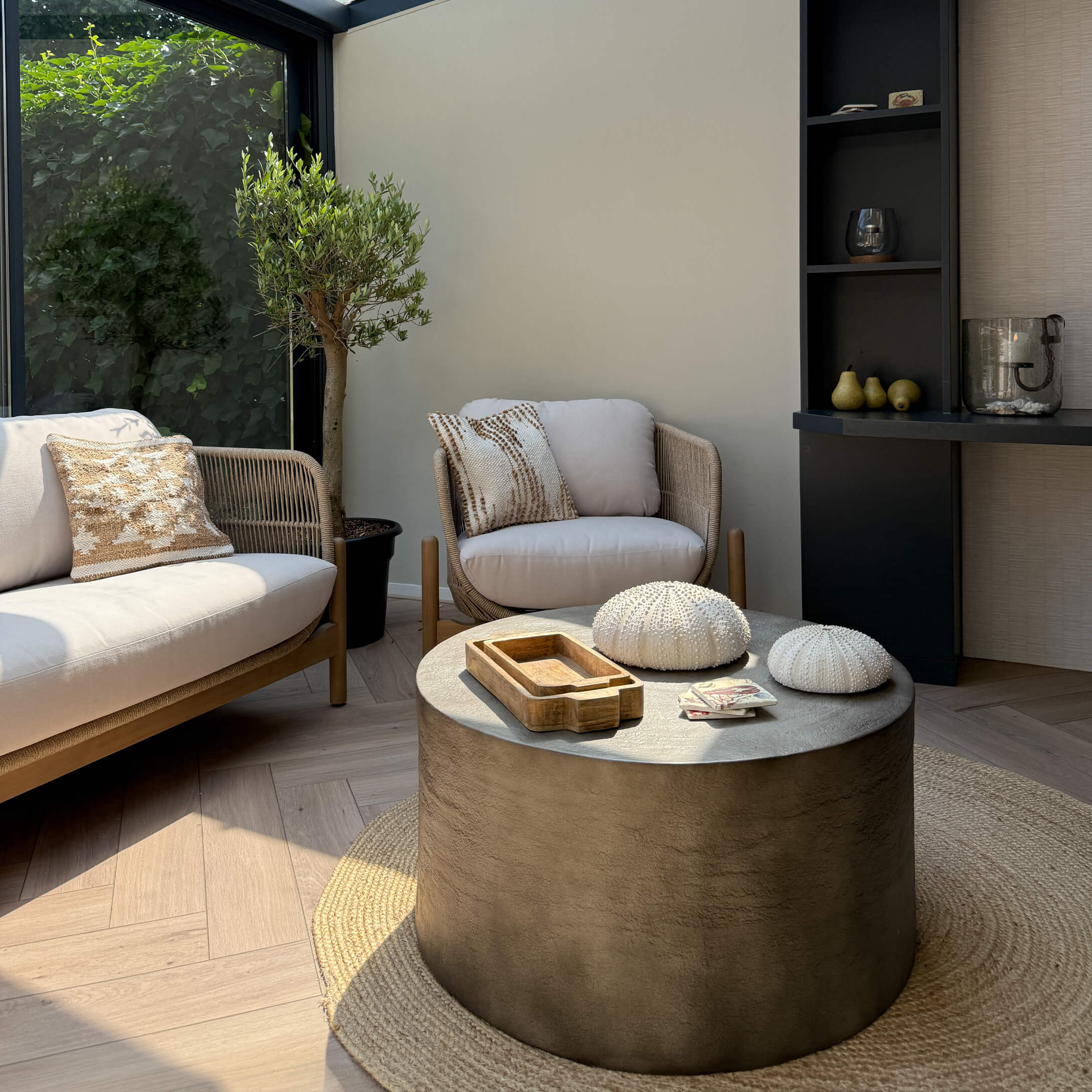 Moderner Wohnbereich mit beigem Sofa und Sessel aus Stoff, runder Beton-Couchtisch auf Naturteppich