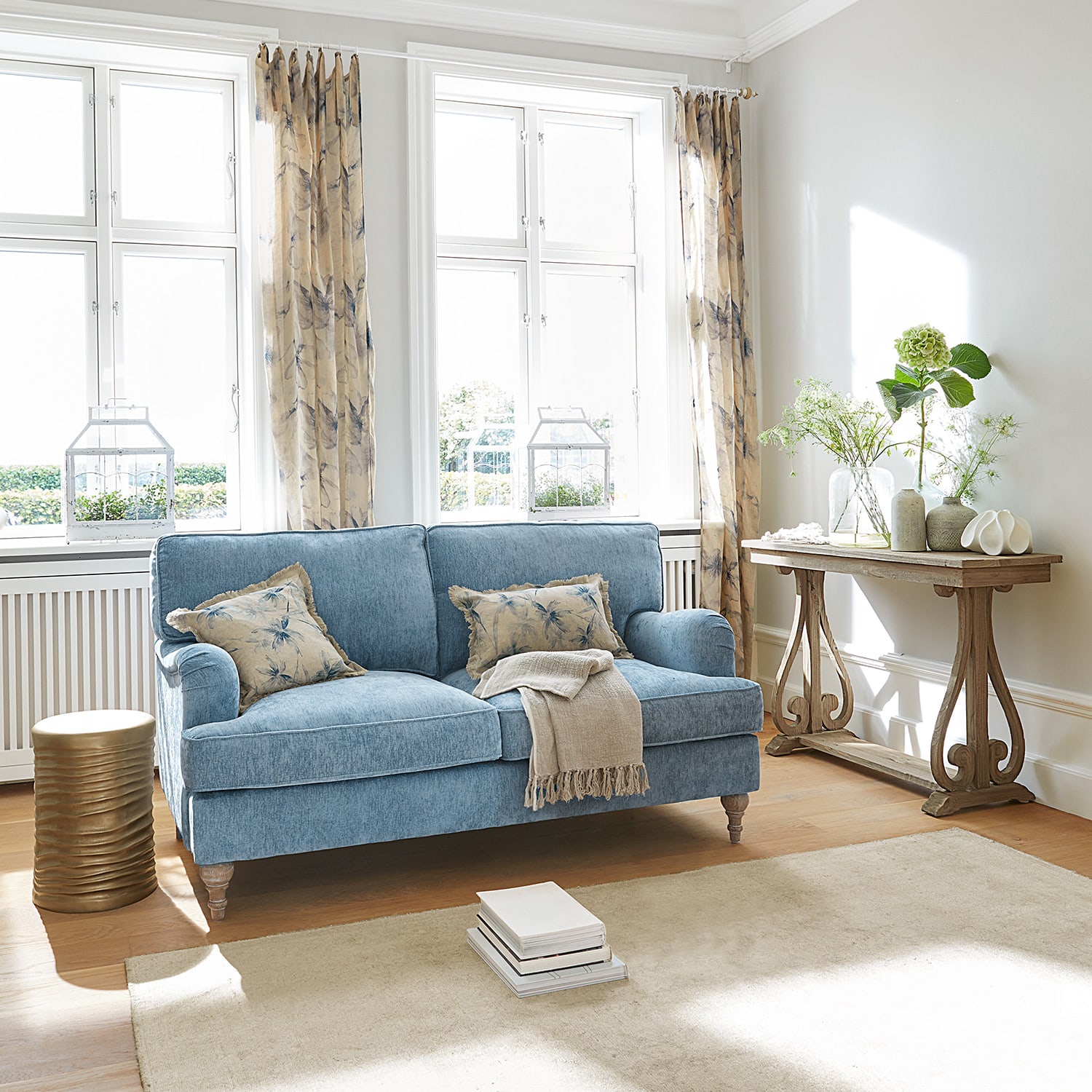 Blau bezogene Couch mit beigen Kissen und Holzkonsole in hellem Wohnzimmer mit Tageslicht
