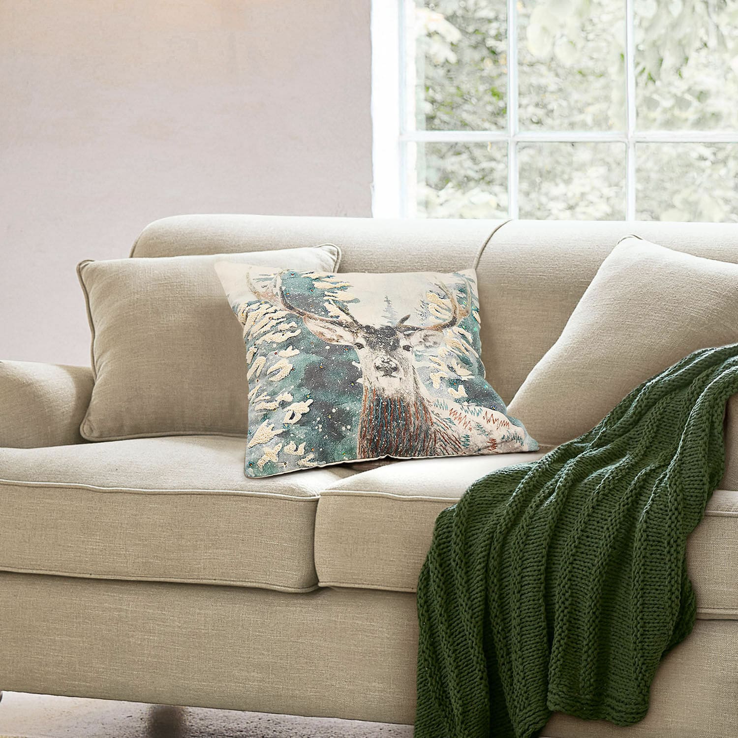 Kissenhülle Elvaris Beiges Sofa mit dekorativem Kissen mit Hirschmotiv und grünem Strickplaid im Wohnzimmer