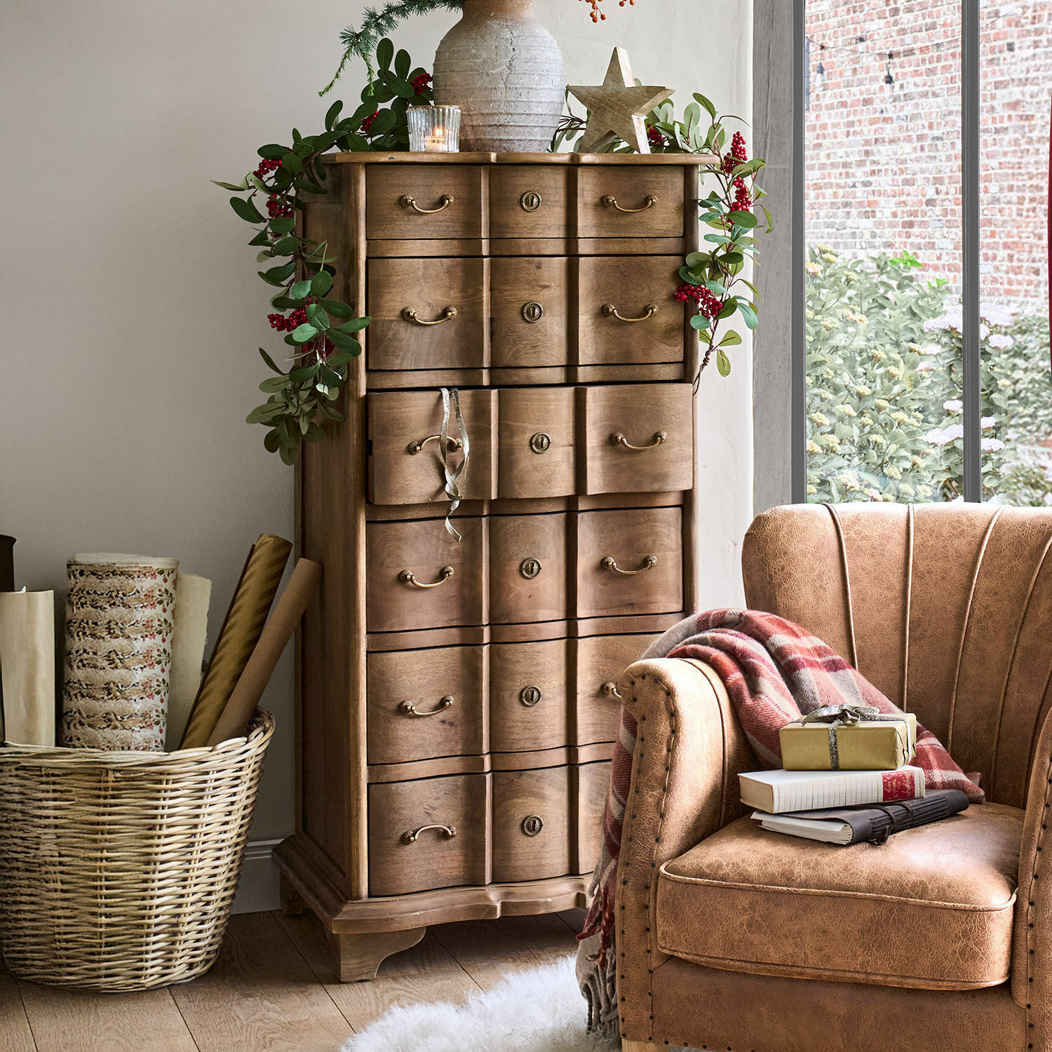 Holzkommode mit dekorativen Griffen und grüner Blattgirlande mit roten Beeren in gemütlichem Raum