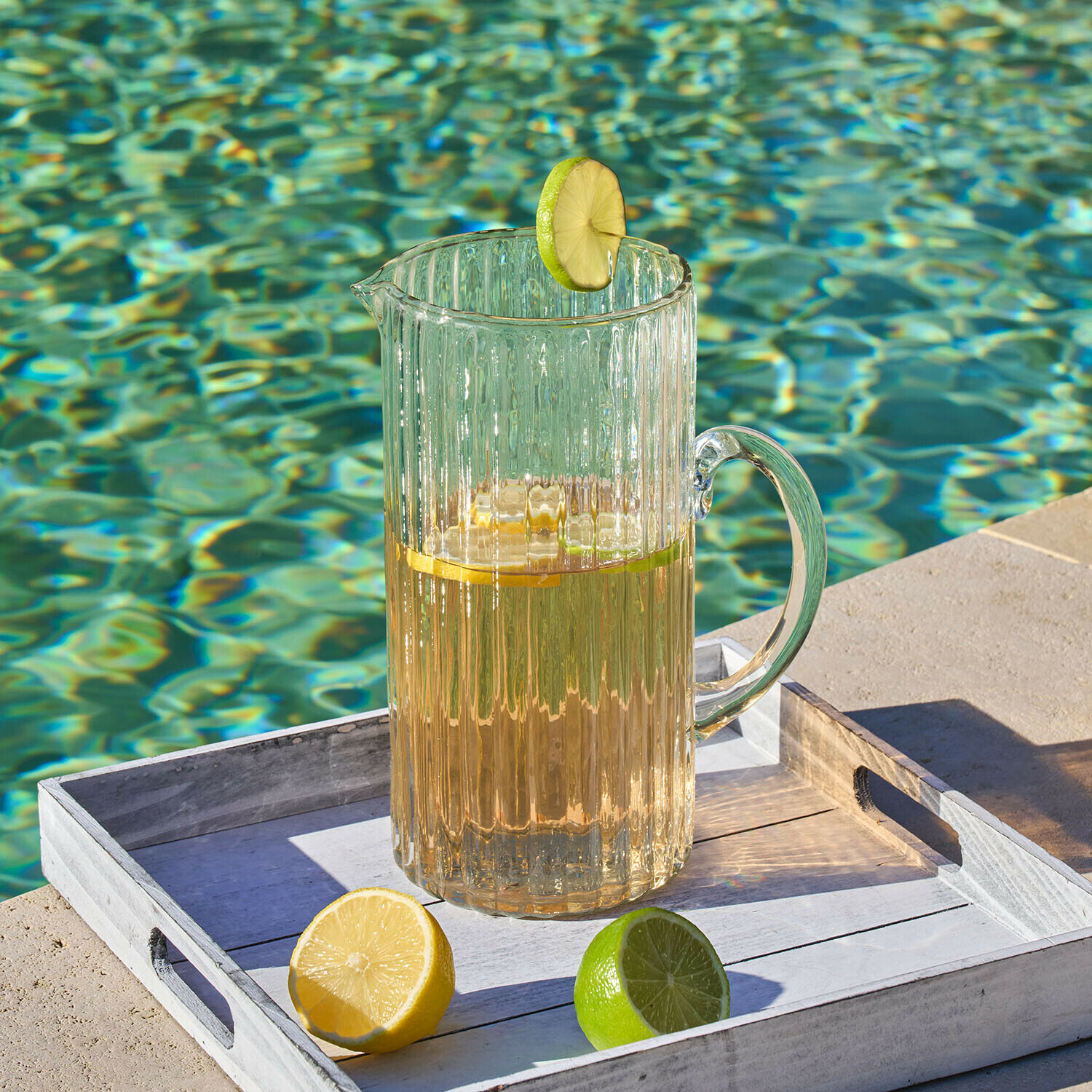 Krug Solerón Transparenter Glas-Krug mit Getränk und Limettenscheibe auf weißem Tablett am Poolrand