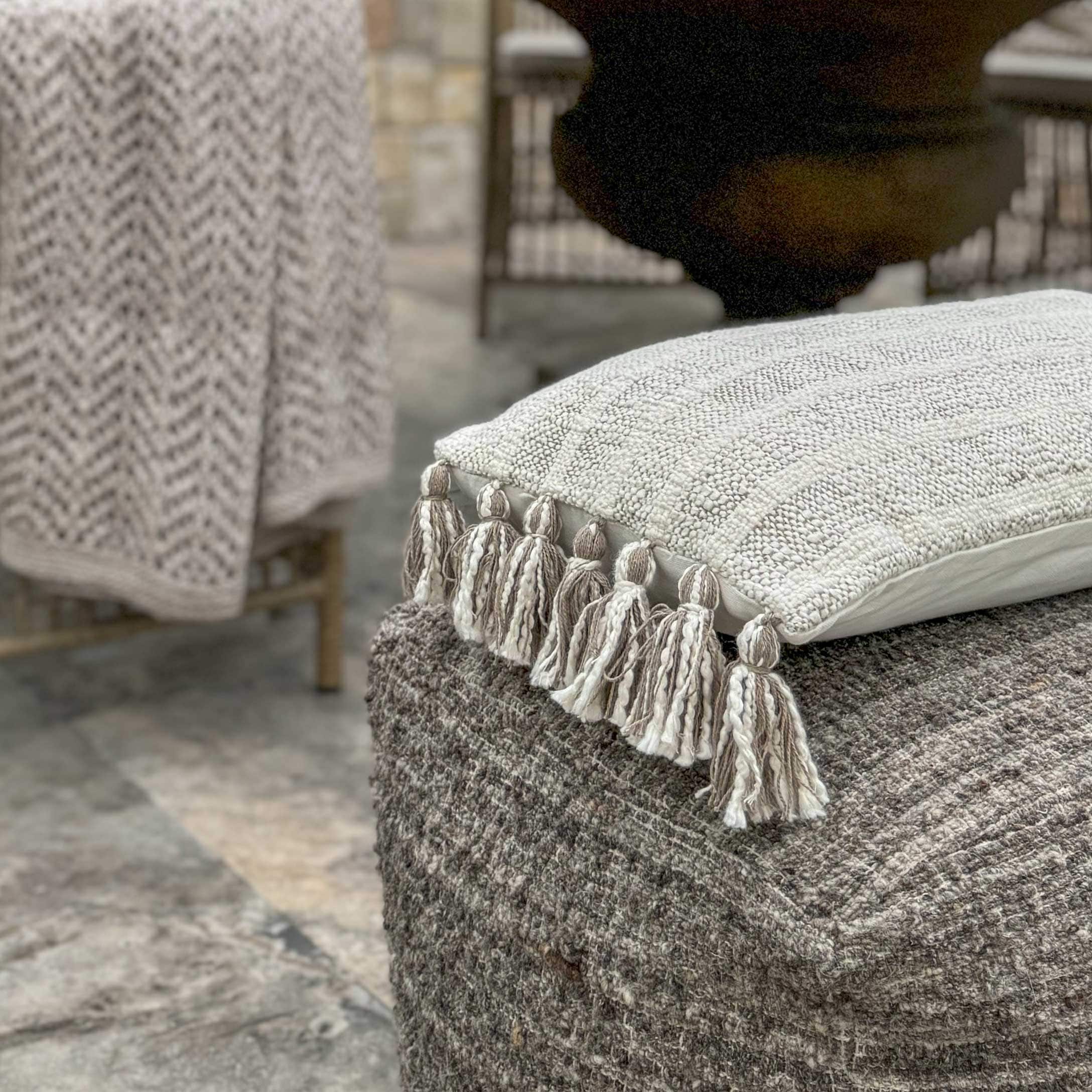 Beige dekoratives Kissen mit Quasten auf grauem Wollhocker, gemütlicher Wohntextilartikel