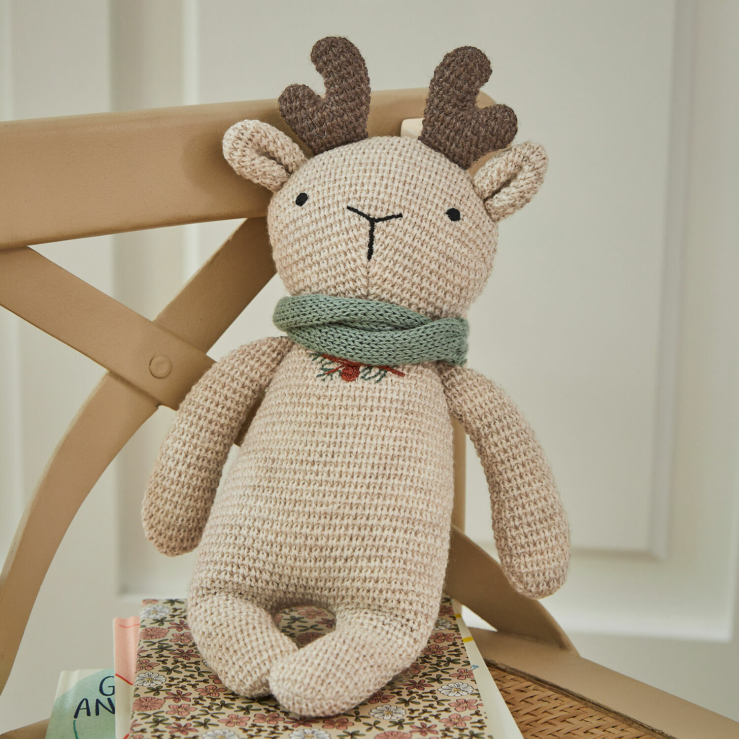 Stofftier Papillia Beige gestricktes Rentier mit braunen Hörnern und grünem Schal auf Stuhl sitzend