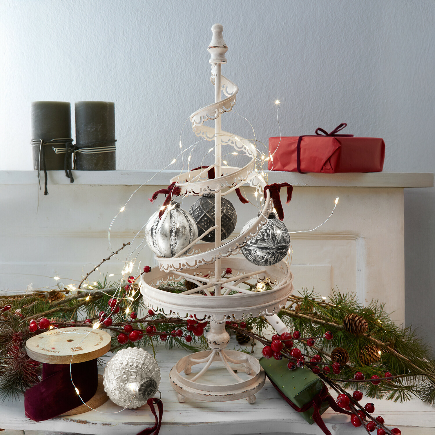 Deko-Baum Gerzat Weiße Metall-Weihnachtsdekoration mit hängenden Kugeln und LED-Lichterkette, rote Geschenke und Tannenzweige im Hintergrund