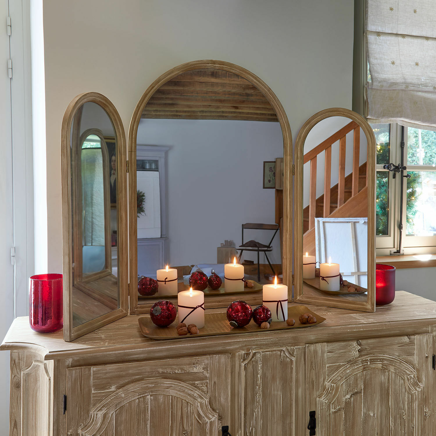 Dreiteiliges Holzspiegel auf Kommode mit brennenden Kerzen und roten Weihnachtskugeln dekoriert