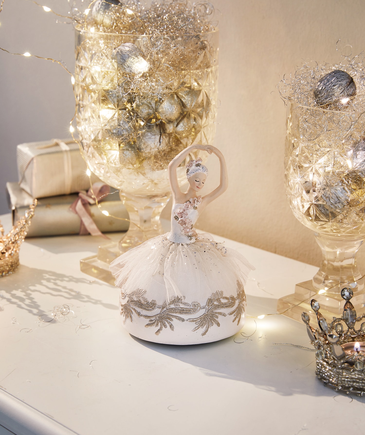 Ballerina-Figur aus Stoff in Creme auf dekorativem Tisch mit Lichterkette und Geschenken