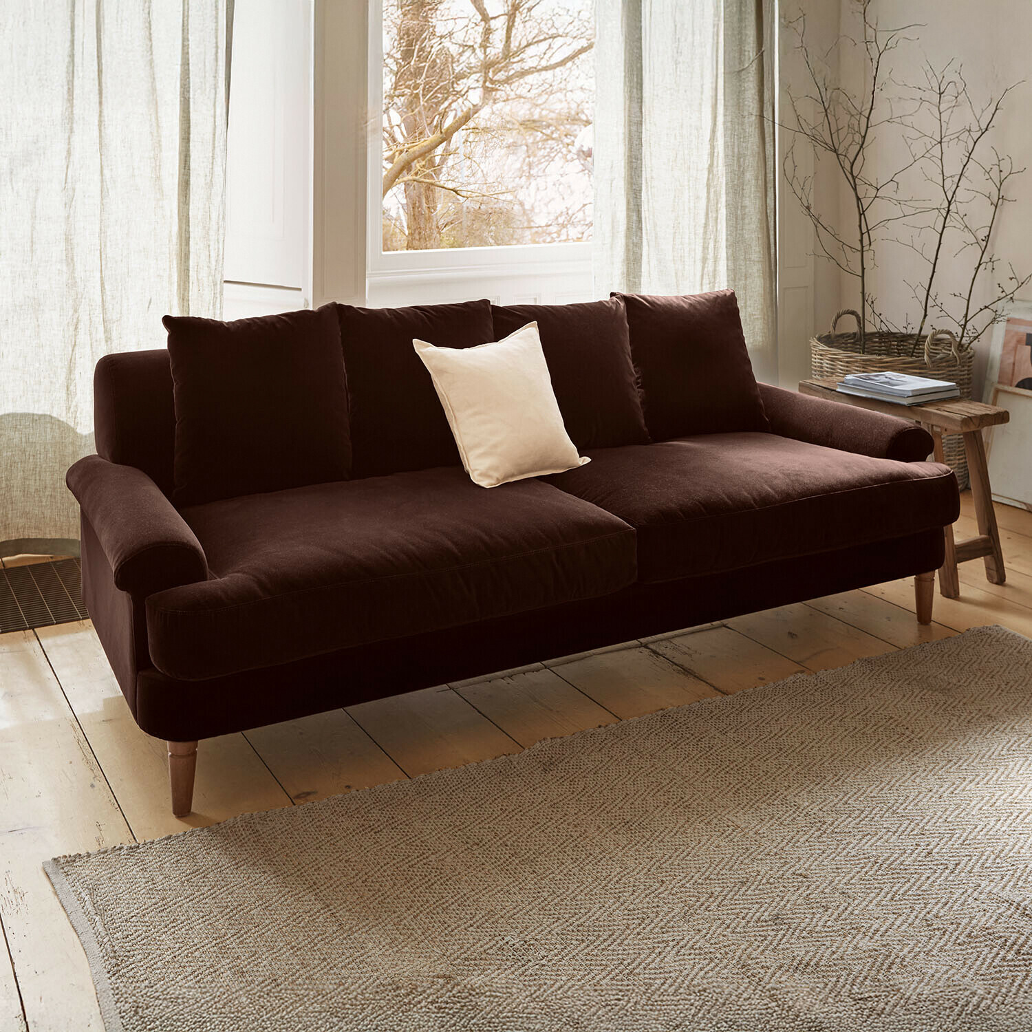 Sofa Rivermere Braunes Samtsofa mit hellem Kissen in gemütlichem Wohnzimmer mit natürlichem Licht