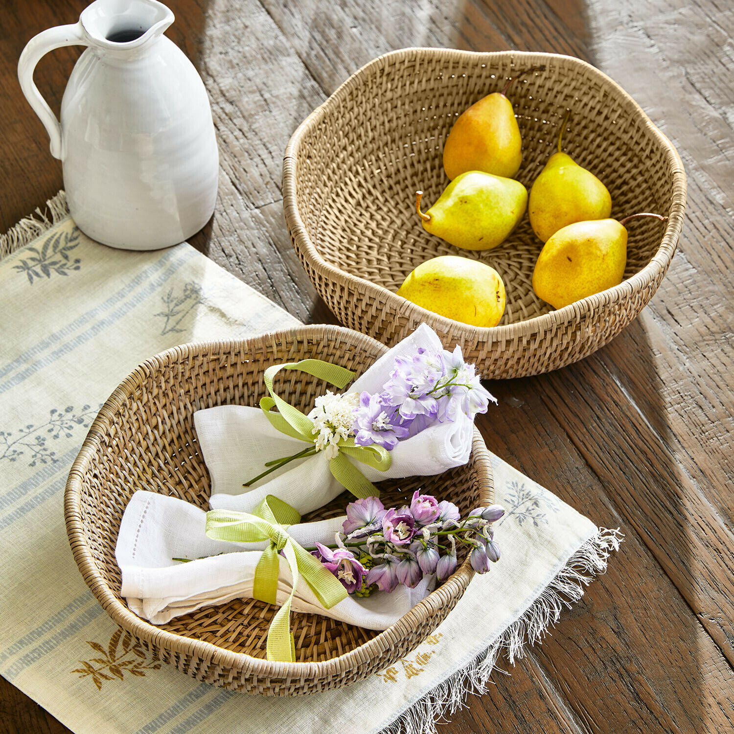 Zwei runde Rattankörbe auf Holztisch, einer mit Birnen, der andere mit Servietten und Blumen dekoriert