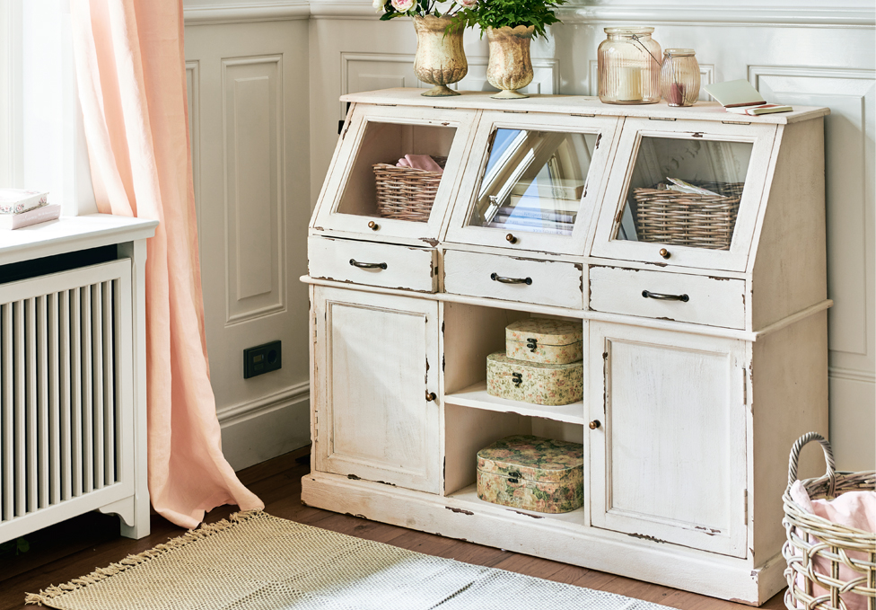 Weißer Holzschrank im Shabby-Chic-Stil mit Glastüren und Dekorationen in einem hellen Raum.