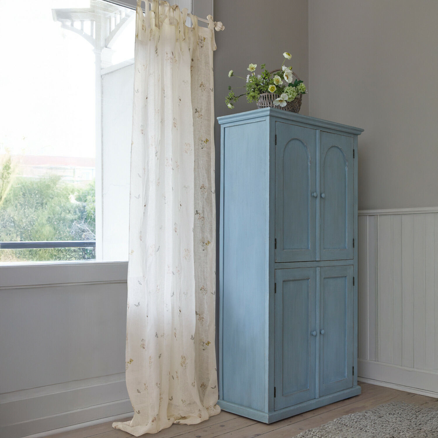 Blauer Holzschrank mit vier Türen und dekorativem Blumenkorb in hellem Raum