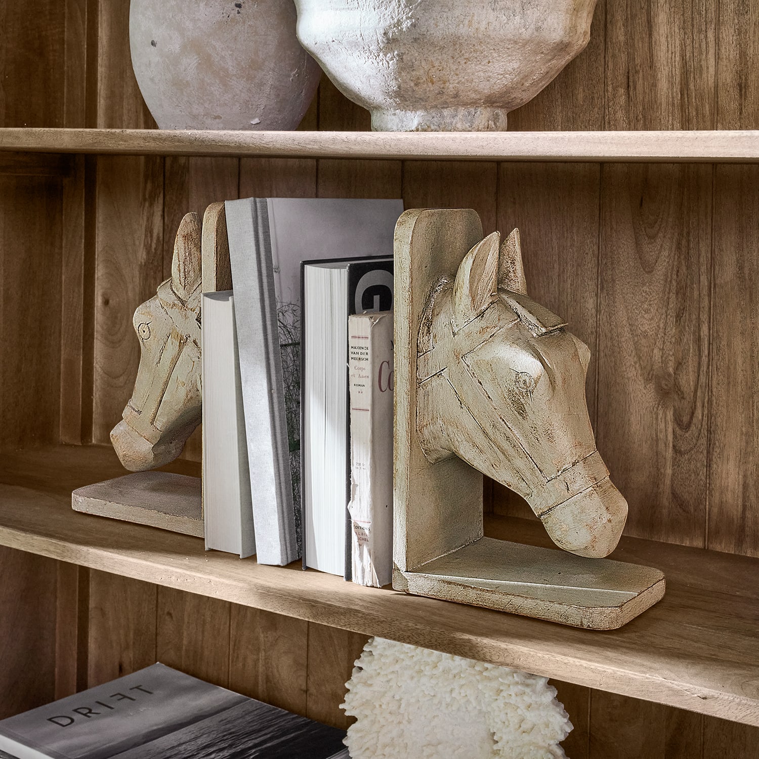 Paar beige Holz-Buchstützen mit Pferdekopf-Motiv auf einem Holzregal mit Büchern