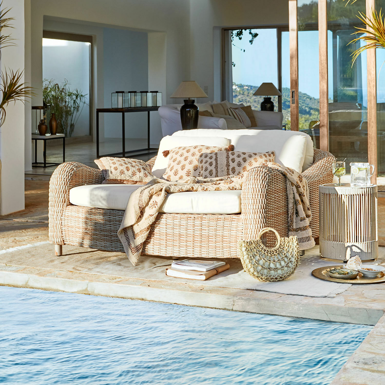 Lounger Heloite Natürliches Rattansofa mit cremefarbenen Kissen und Decke am Pool in modernem Wohnraum