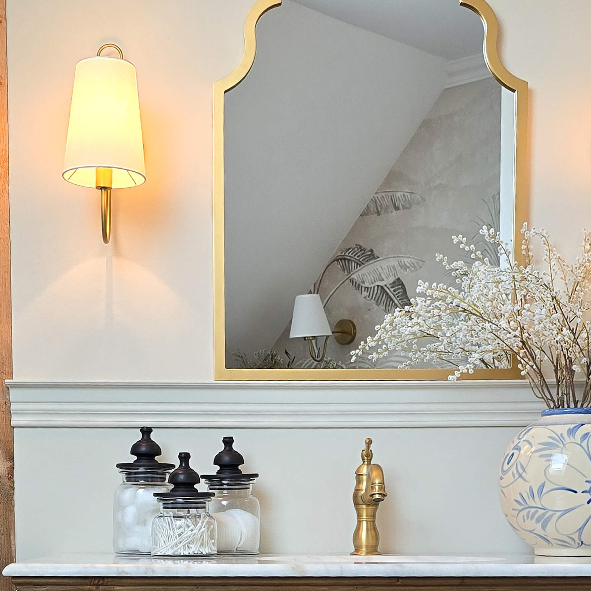 Goldgerahmter Spiegel über Marmorwaschbecken mit Messingarmatur und Glasbehältern im Bad