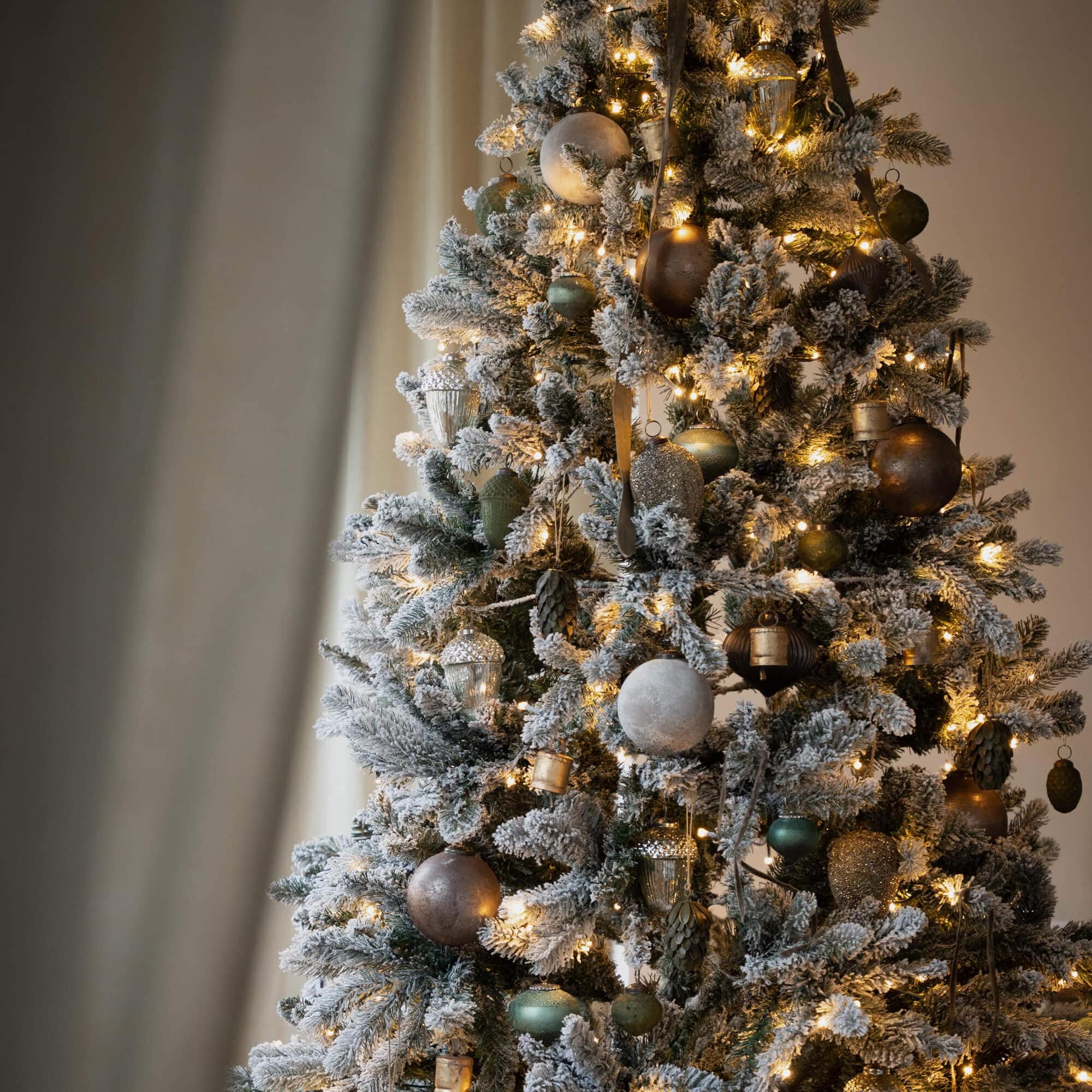 Künstlicher Weihnachtsbaum mit Schneeeffekt und gold-grünen Kugeln, beleuchtet für festliche Stimmung