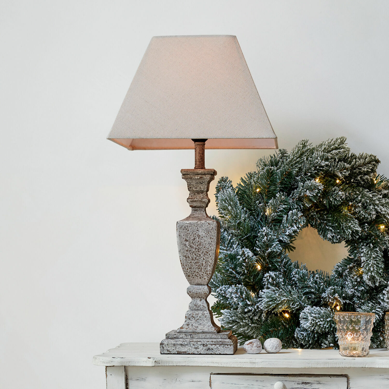 Tischlampe Gorham Beige Steintischlampe mit Lampenschirm neben grünem Weihnachtskranz mit Lichterkette auf weißem Tisch