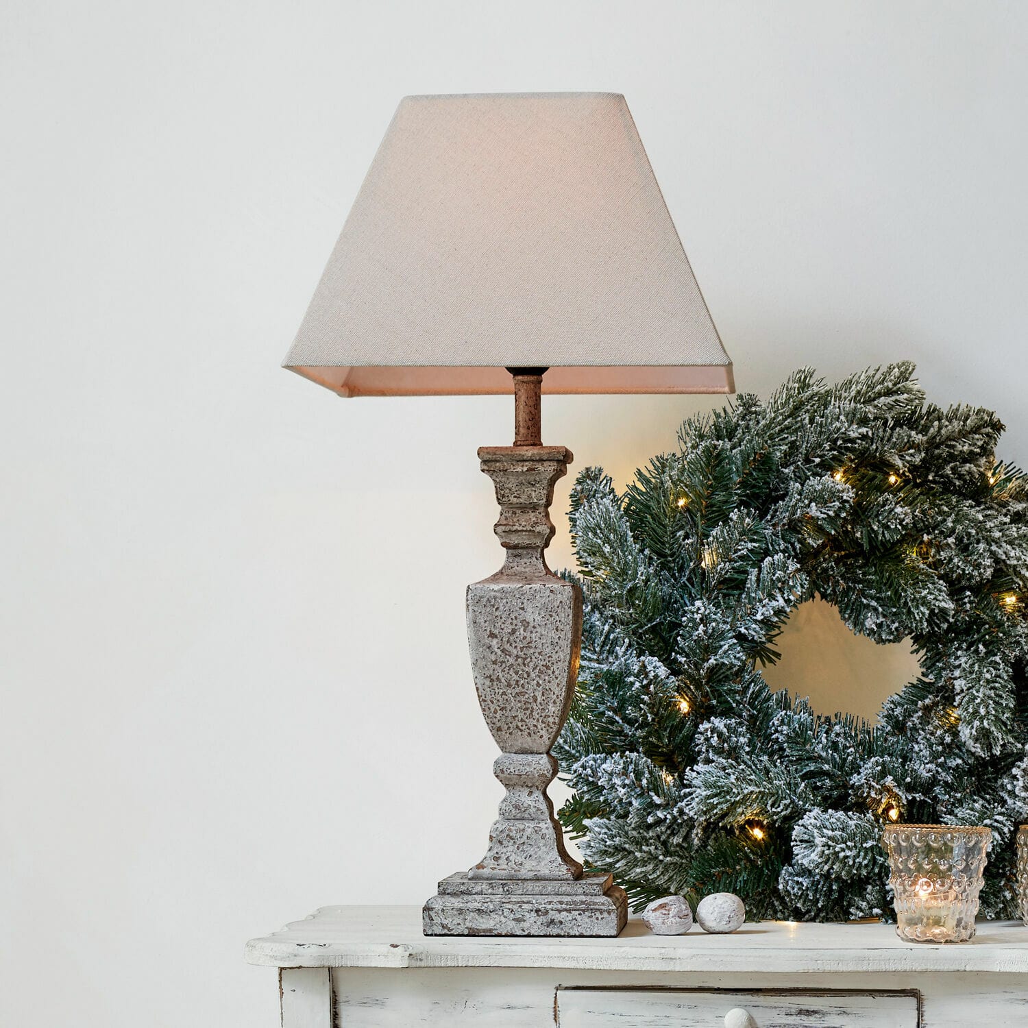 Tischlampe Gorham Beige Steintischlampe mit Lampenschirm neben grünem Weihnachtskranz mit Lichterkette auf weißem Tisch
