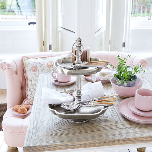 Zweistöckige Metall-Etagere auf Tisch mit rosa Porzellan und grüner Pflanze in hellem Raum