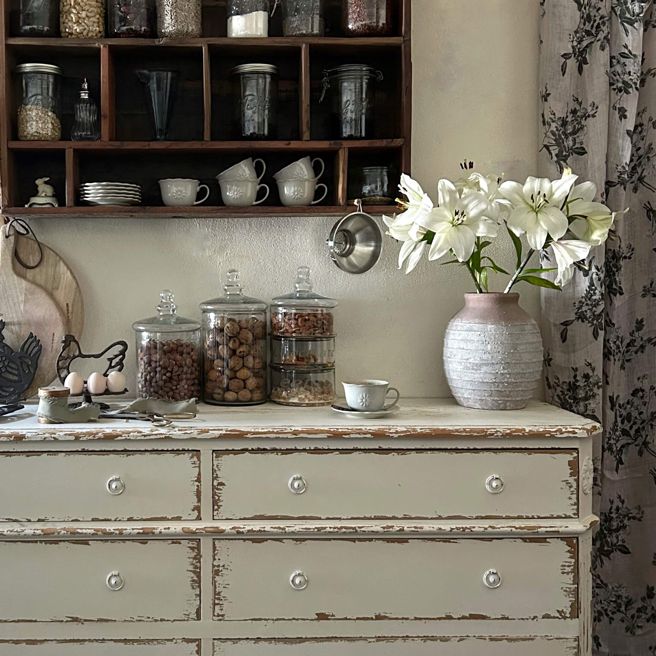 Rustikaler weißer Schrank mit rosa Keramikvase und weißen Lilien in einer Vintage-Küche