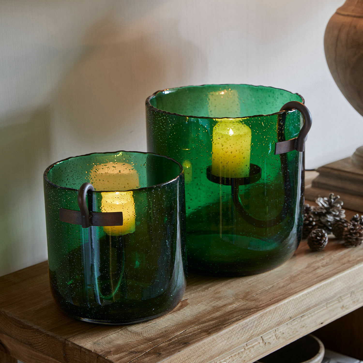 Windlicht 2er Set Ylva Set aus zwei grünen Glaswindlichtern mit Metallgriffen auf einem Holztisch
