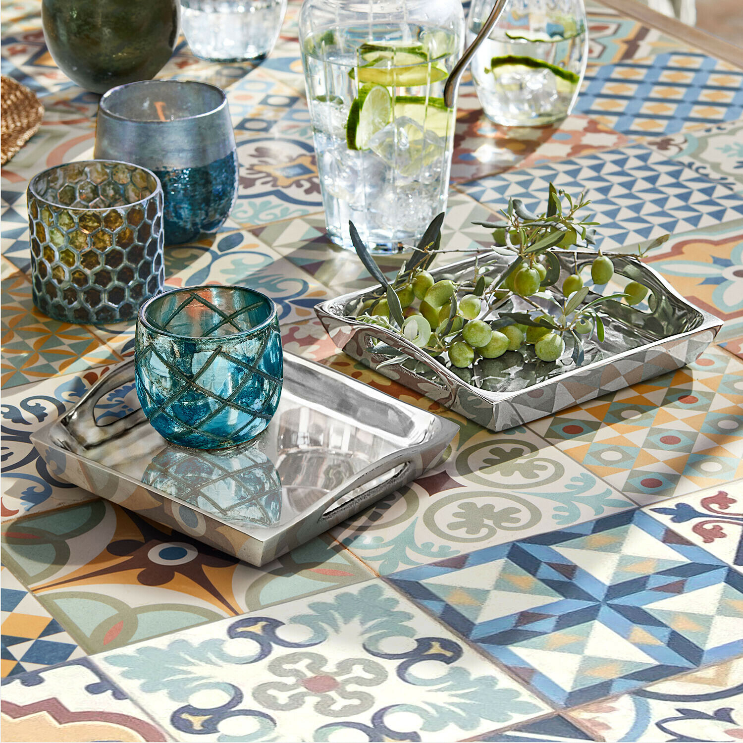 Tablett 2er Set Grélomiane Zweiseitige silberne Metalltabletts auf buntem Mosaiktisch mit blauen Glaswindlichtern und grünen Oliven