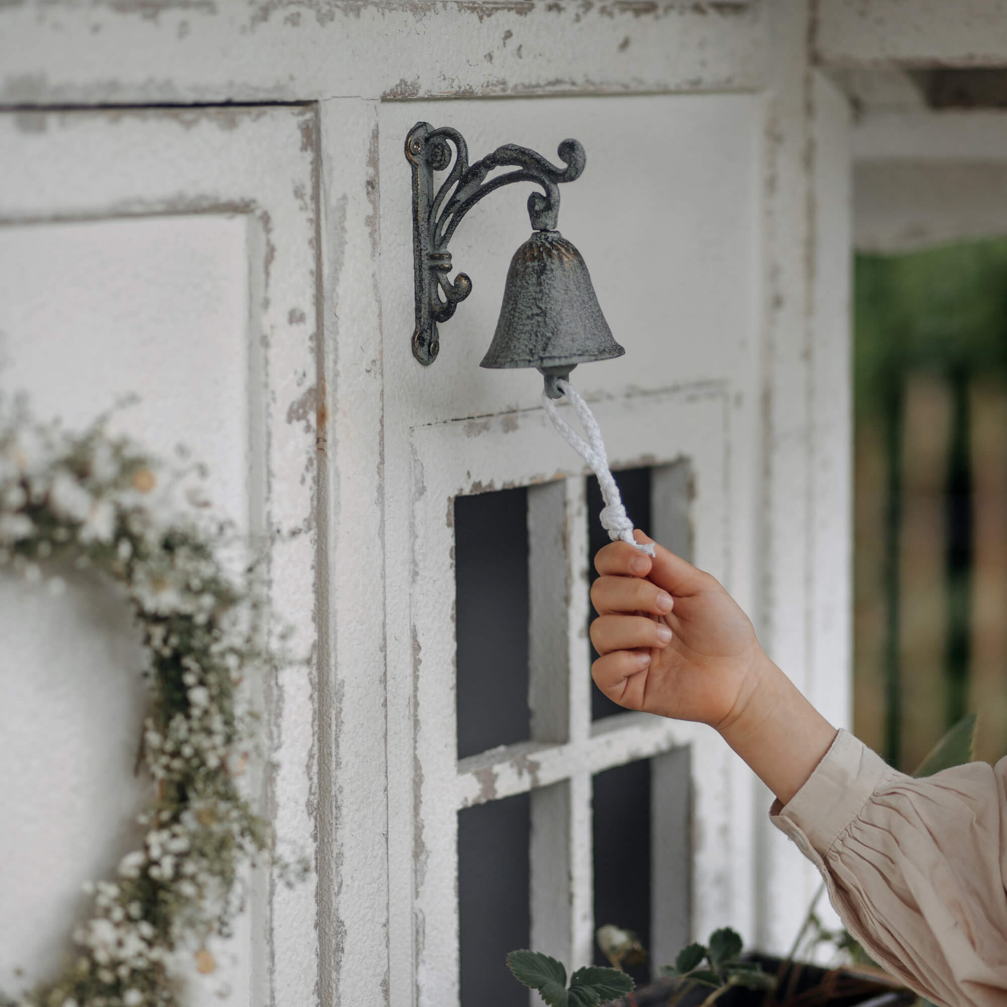 Metallglocke im Vintage-Stil mit weißem Seil an verwitterter Außenwand montiert