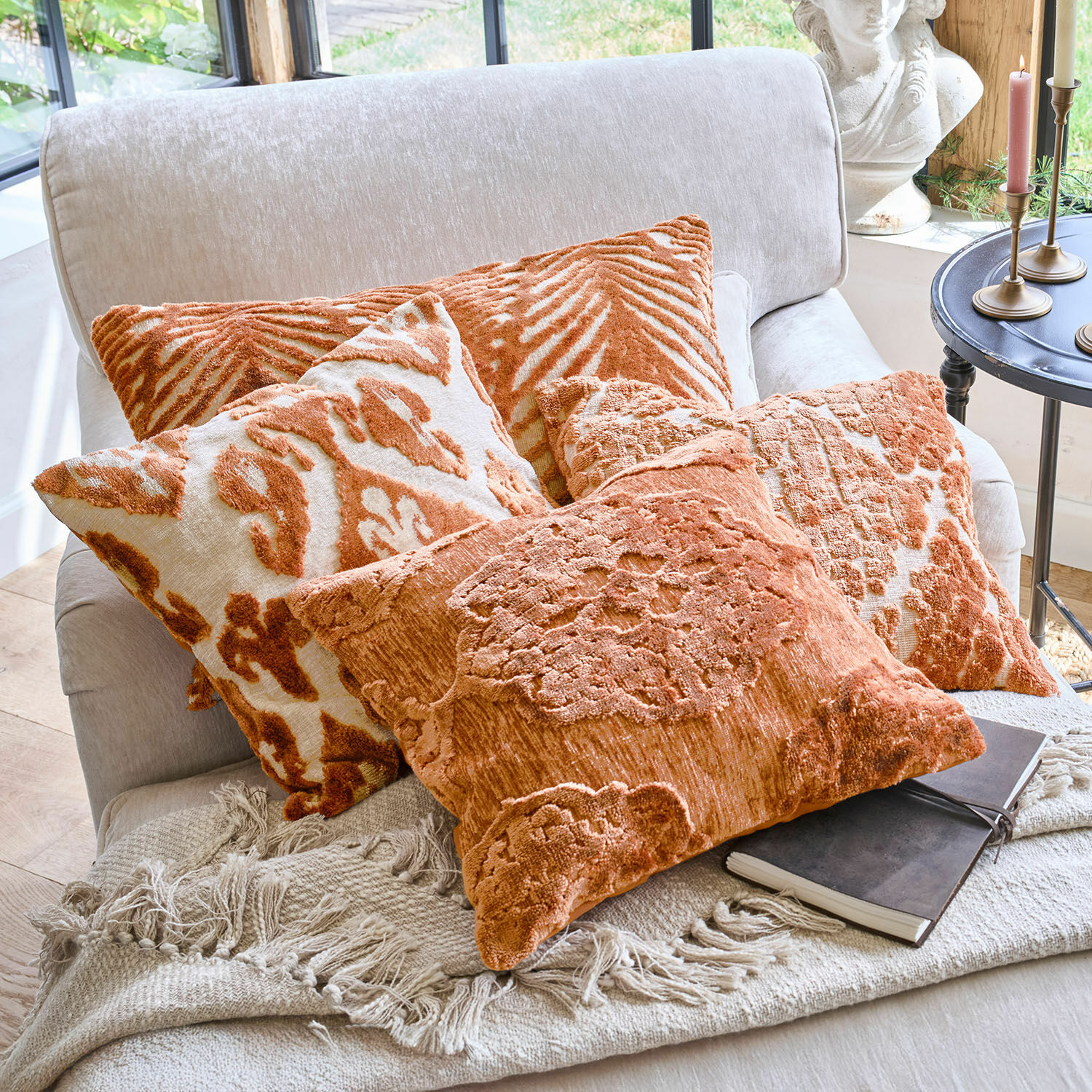 Set aus orangefarbenen Dekokissen mit Mustern auf hellem Sofa mit Fransen-Decke