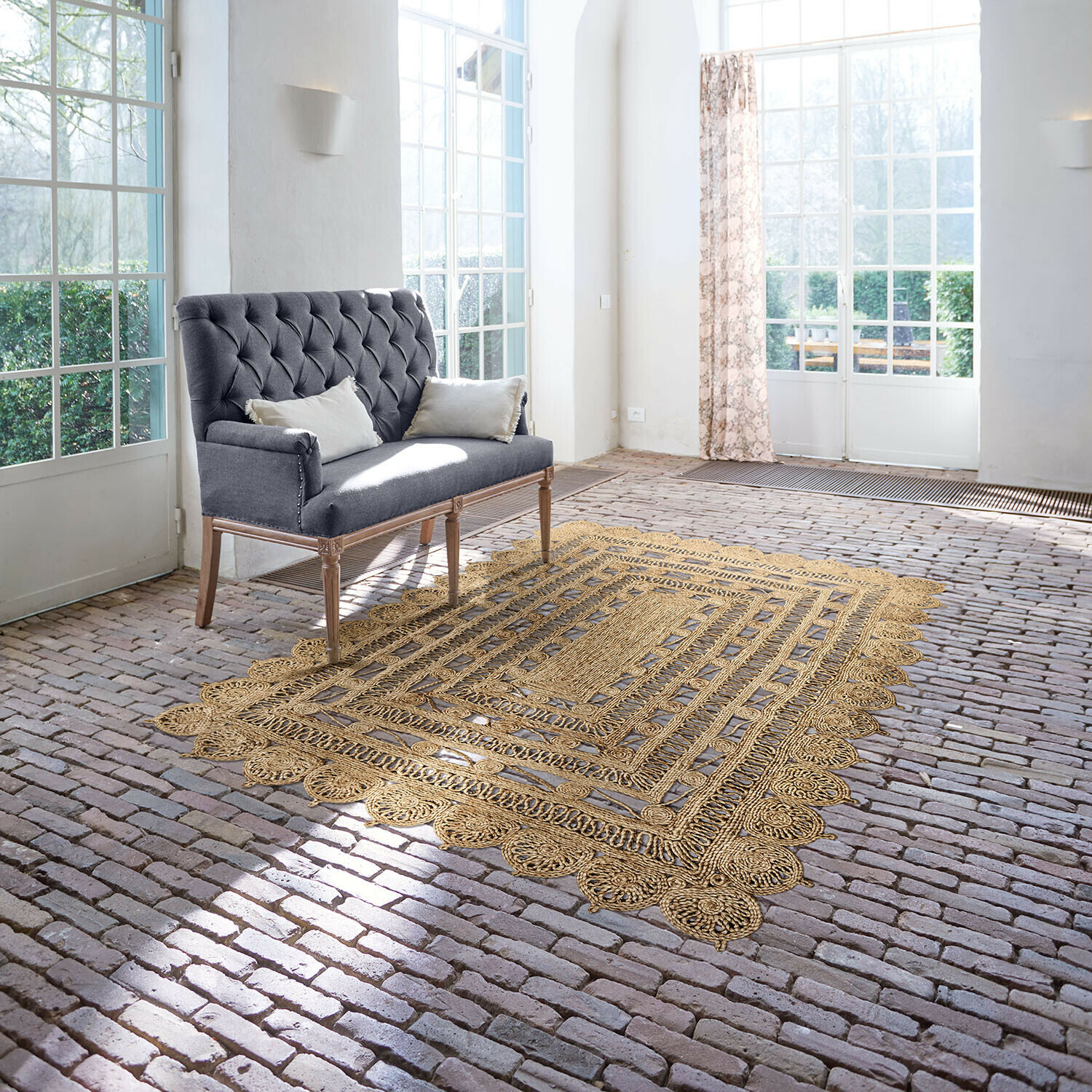 Teppich Livadia Grau gepolsterte Sofa mit Holzbeinen in hellem Raum mit Jute-Teppich auf Ziegelboden