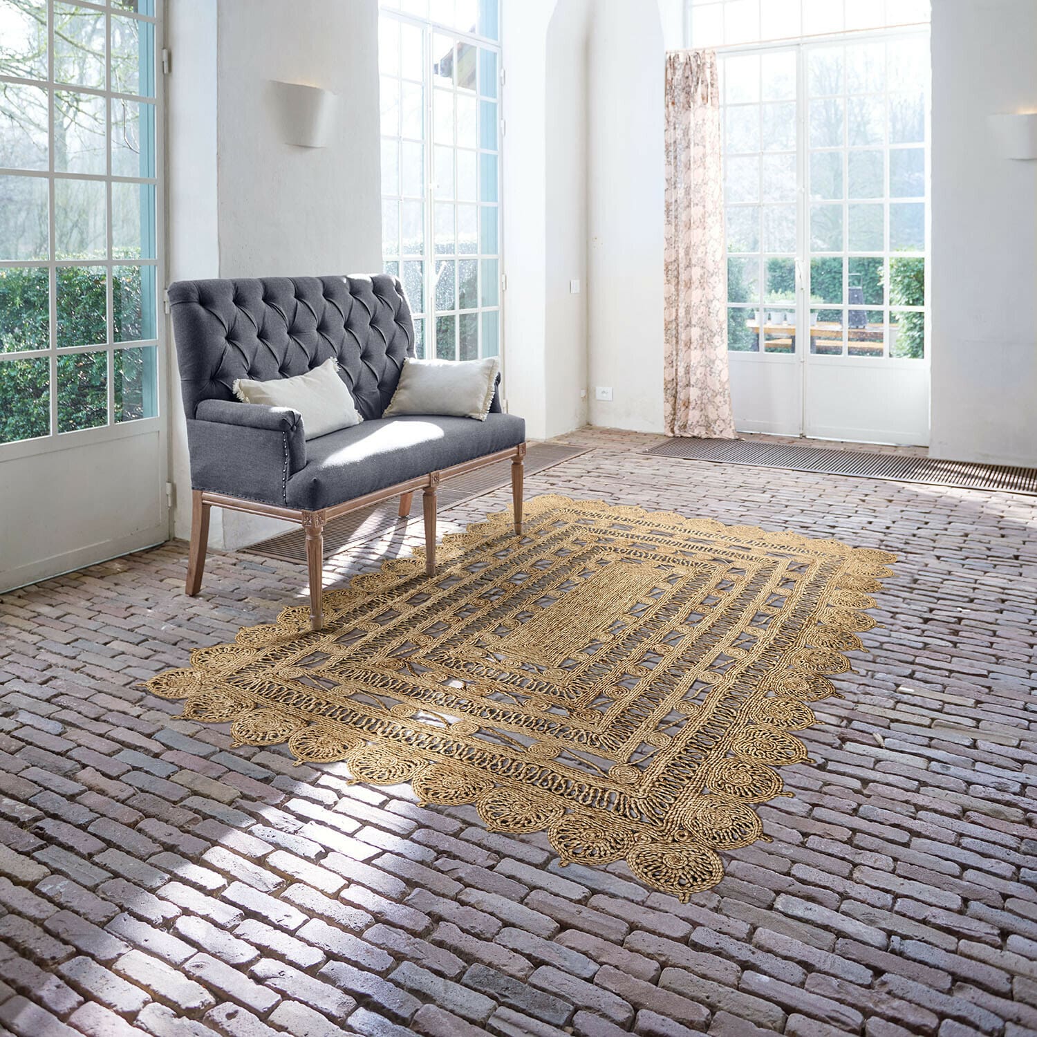 Teppich Livadia Grau gepolsterte Sofa mit Holzbeinen in hellem Raum mit Jute-Teppich auf Ziegelboden