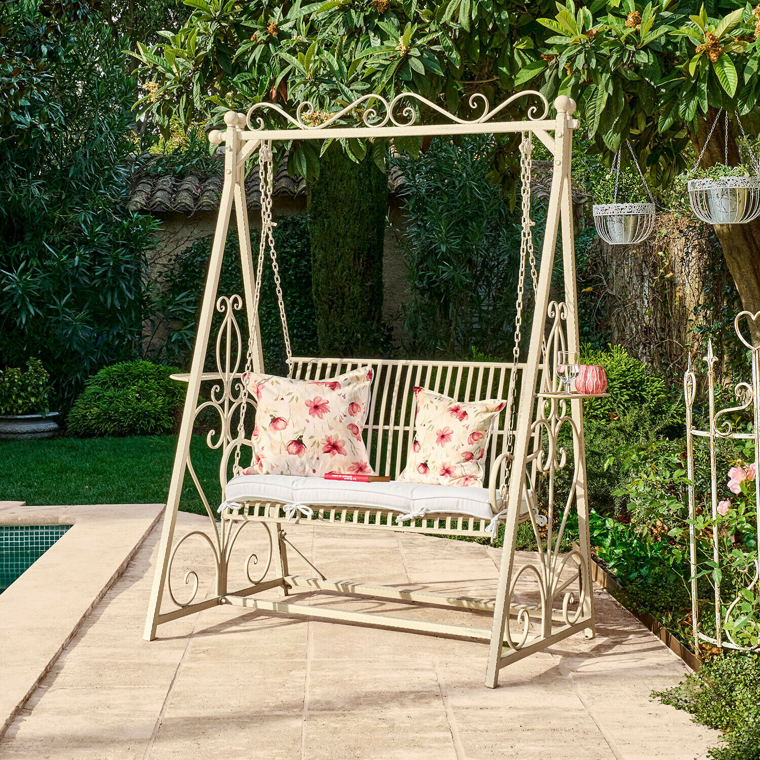 Metall-Gartenschaukel in Creme mit floral gemusterten Kissen auf Terrasse neben Pool